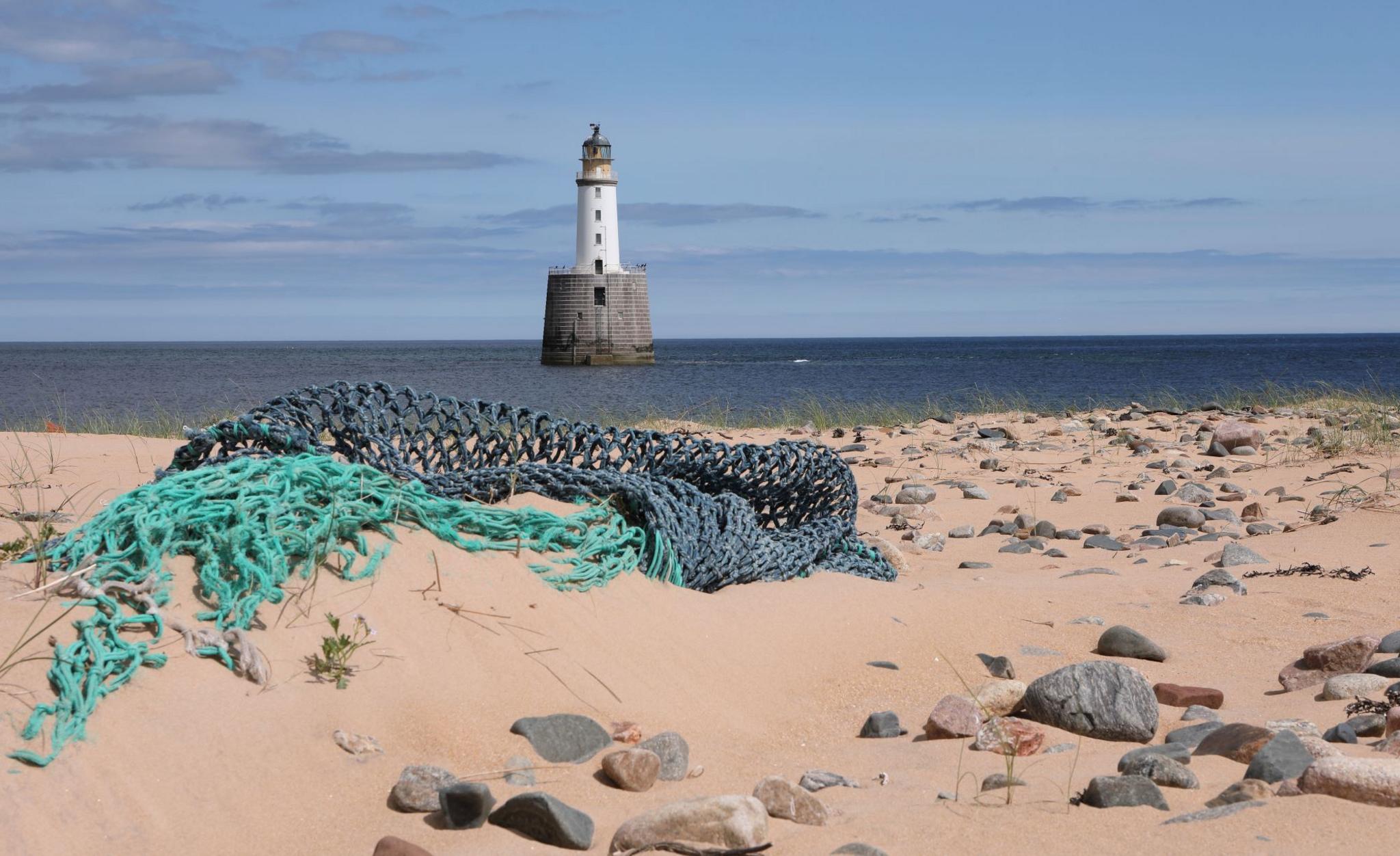 Sandy beach with two fishing nets and rocks scattered and a white lighthouse in the distance