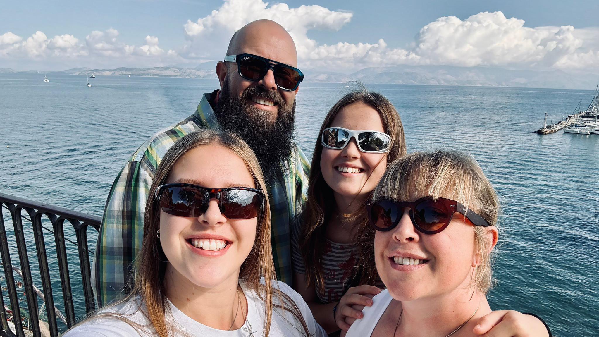 Faye's daughter is taking a family selfie. There are four people in the image: Faye's husband and two daughters, with the sea behind them. 