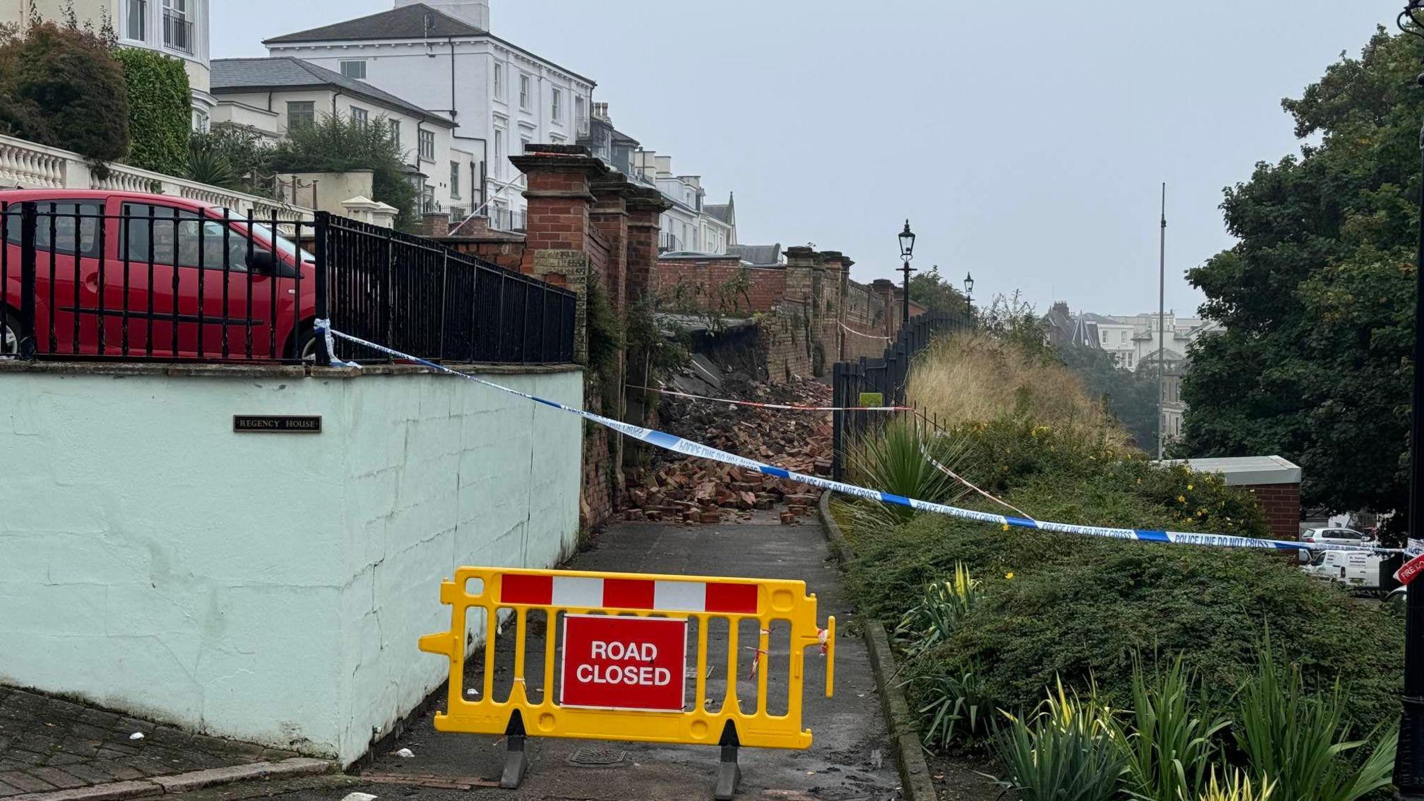 A 'road closed' sign blocking a pathway where a wall has collapsed. 