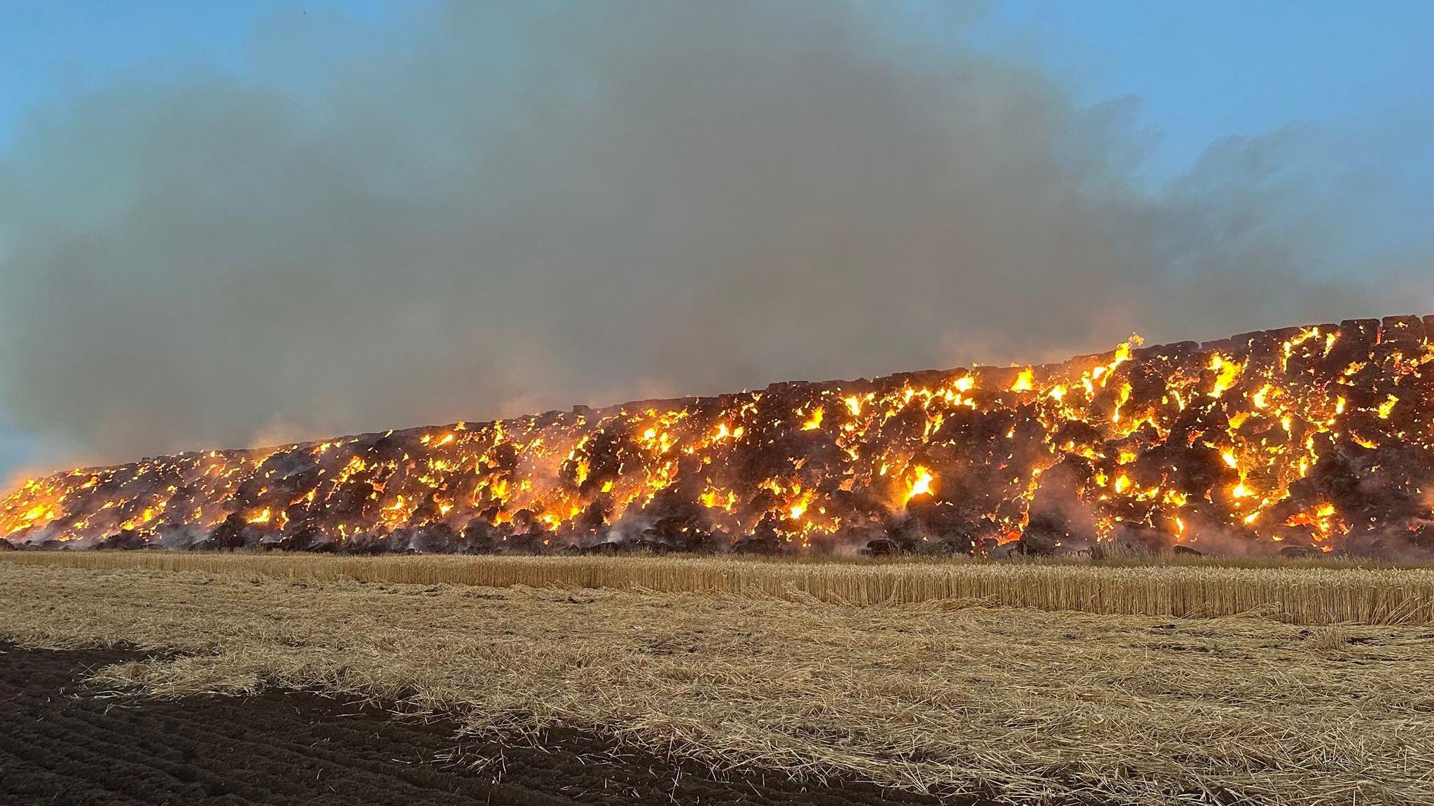 A large pile of hay bales on fire.