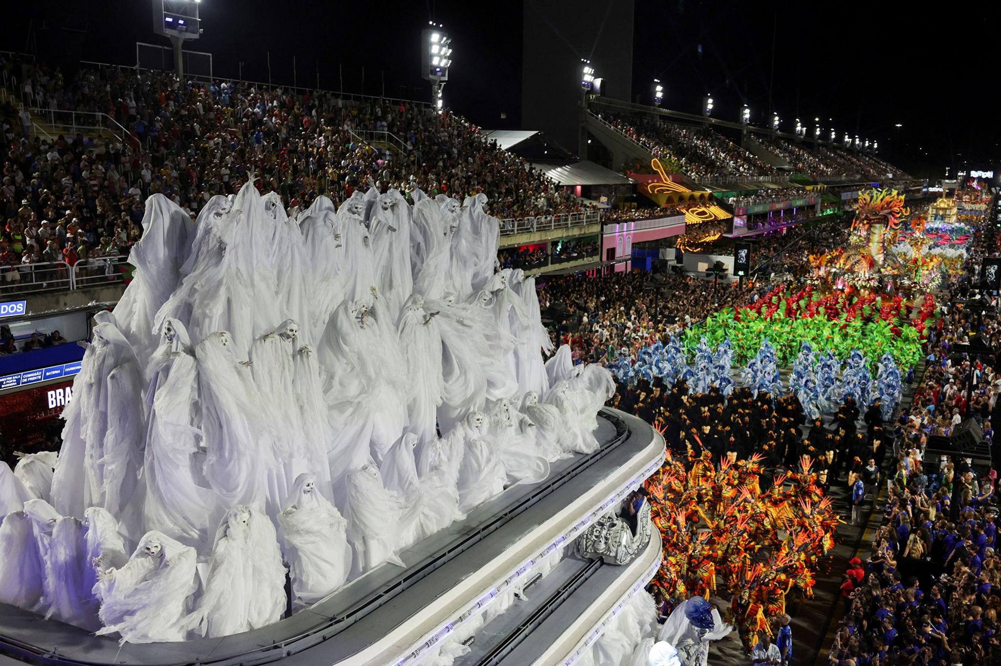 Revellers dressed as ghosts from Vila Isabel samba school perform against the wider backdrop of the Sambadrome