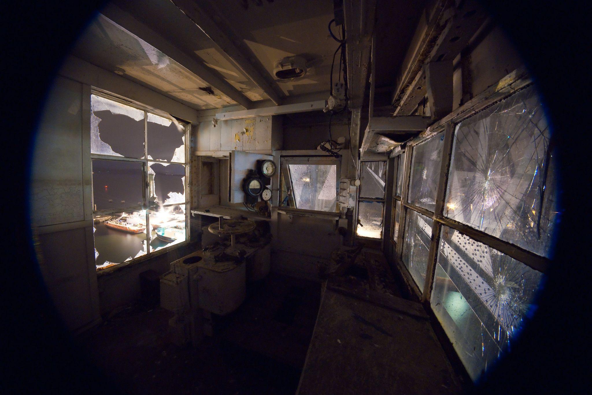 The interior of the crane's cab. The glass is broken in some of the windows and dials can be viewed as part of the equipment.