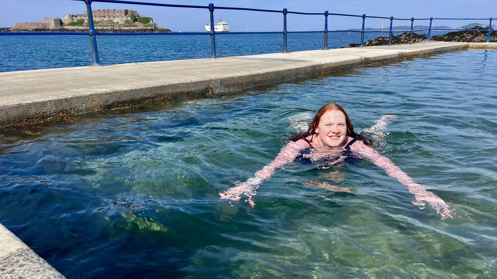 Alice swims in a sea pool along the Guernsey coast. She is looking directly at the camera and is smiling.