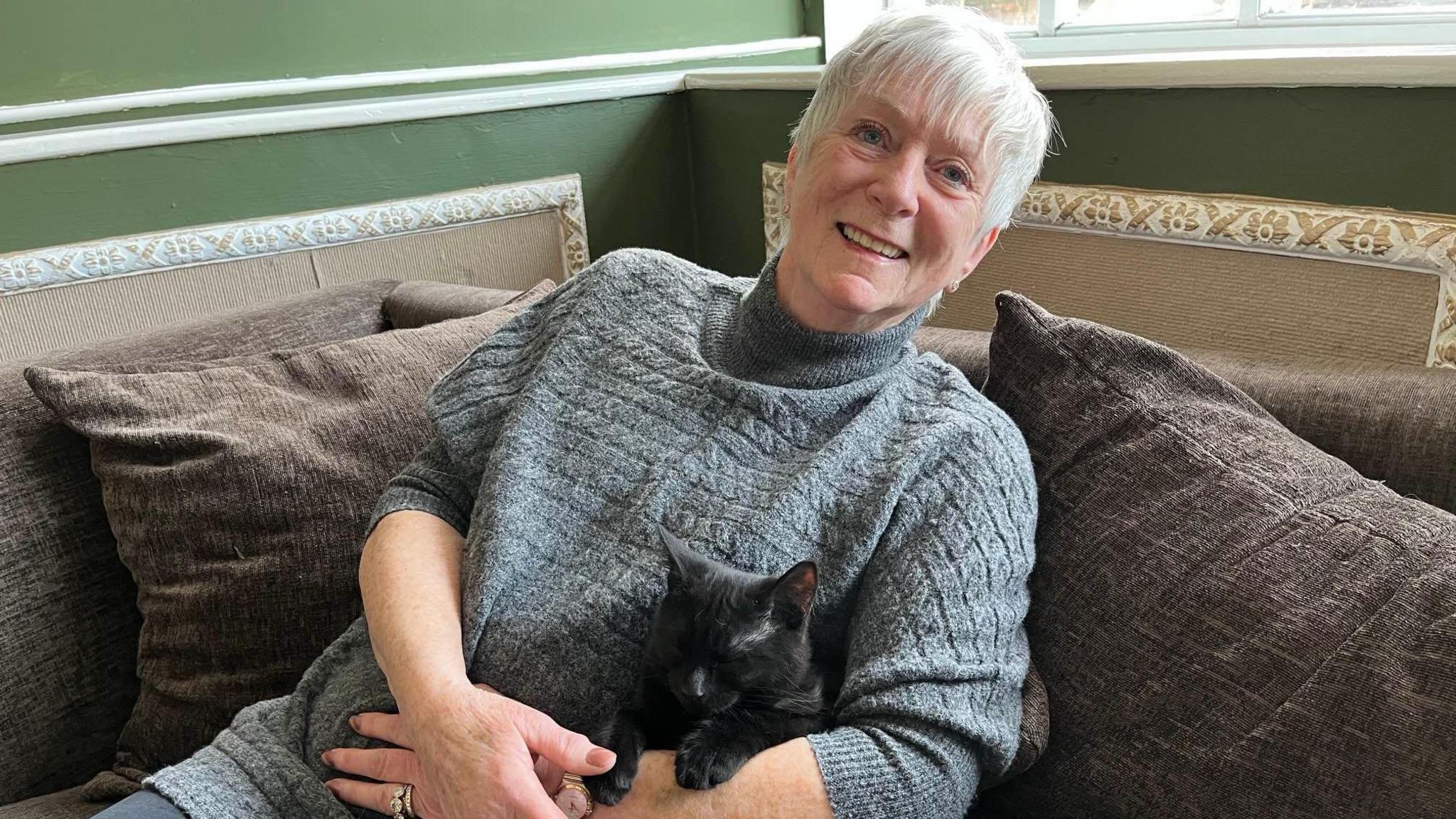 Iris Smith, cat cafe customer, is sat on a sofa cuddling a black rescue kitten