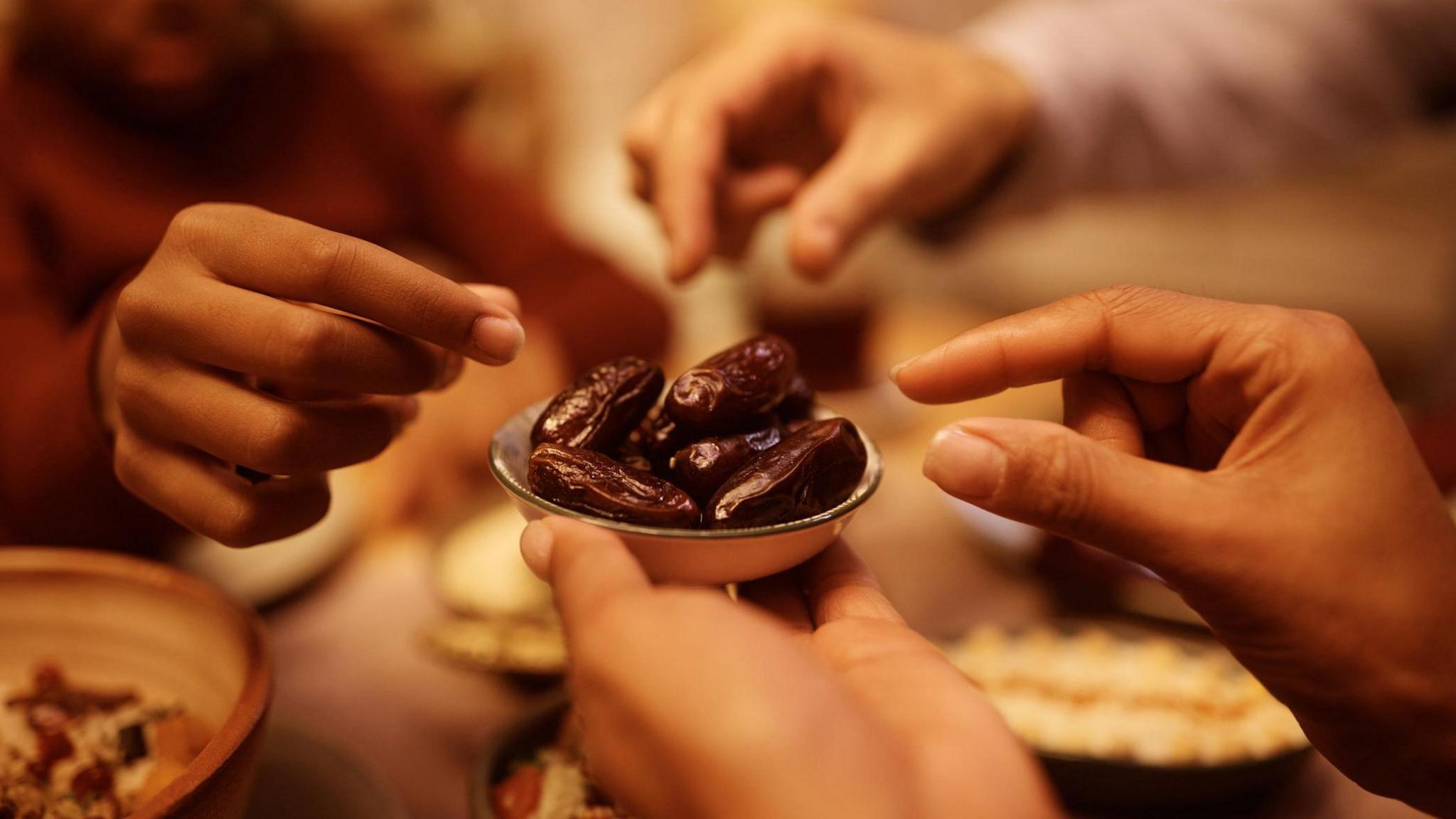 Close up of a family reaching for dates from a plate at the start of iftar