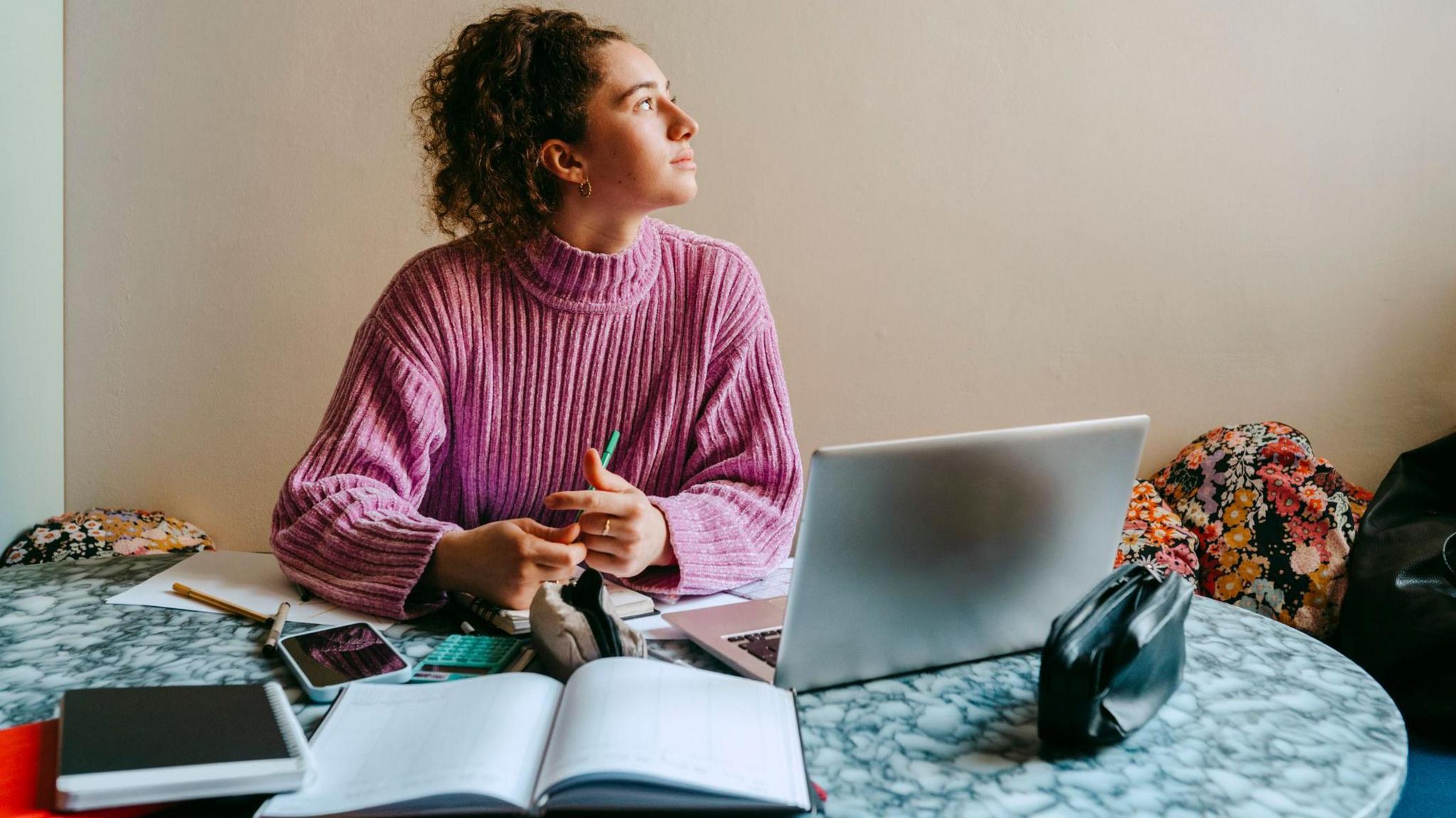 Woman reflecting by looking out of a window while sitting at her laptop