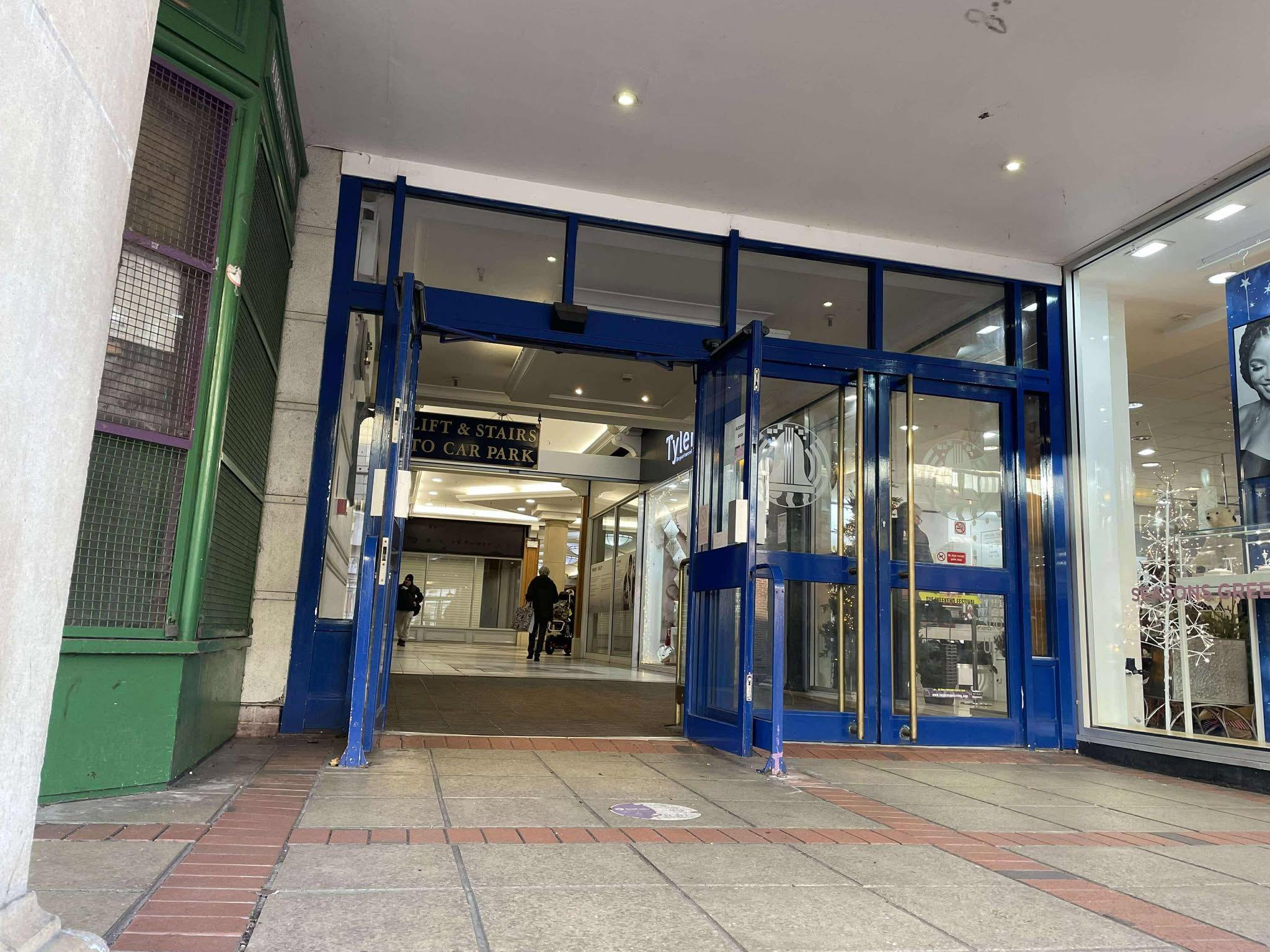 A view through the doors of Carillon Court with a few shoppers walking swiftly through a corridor of empty units