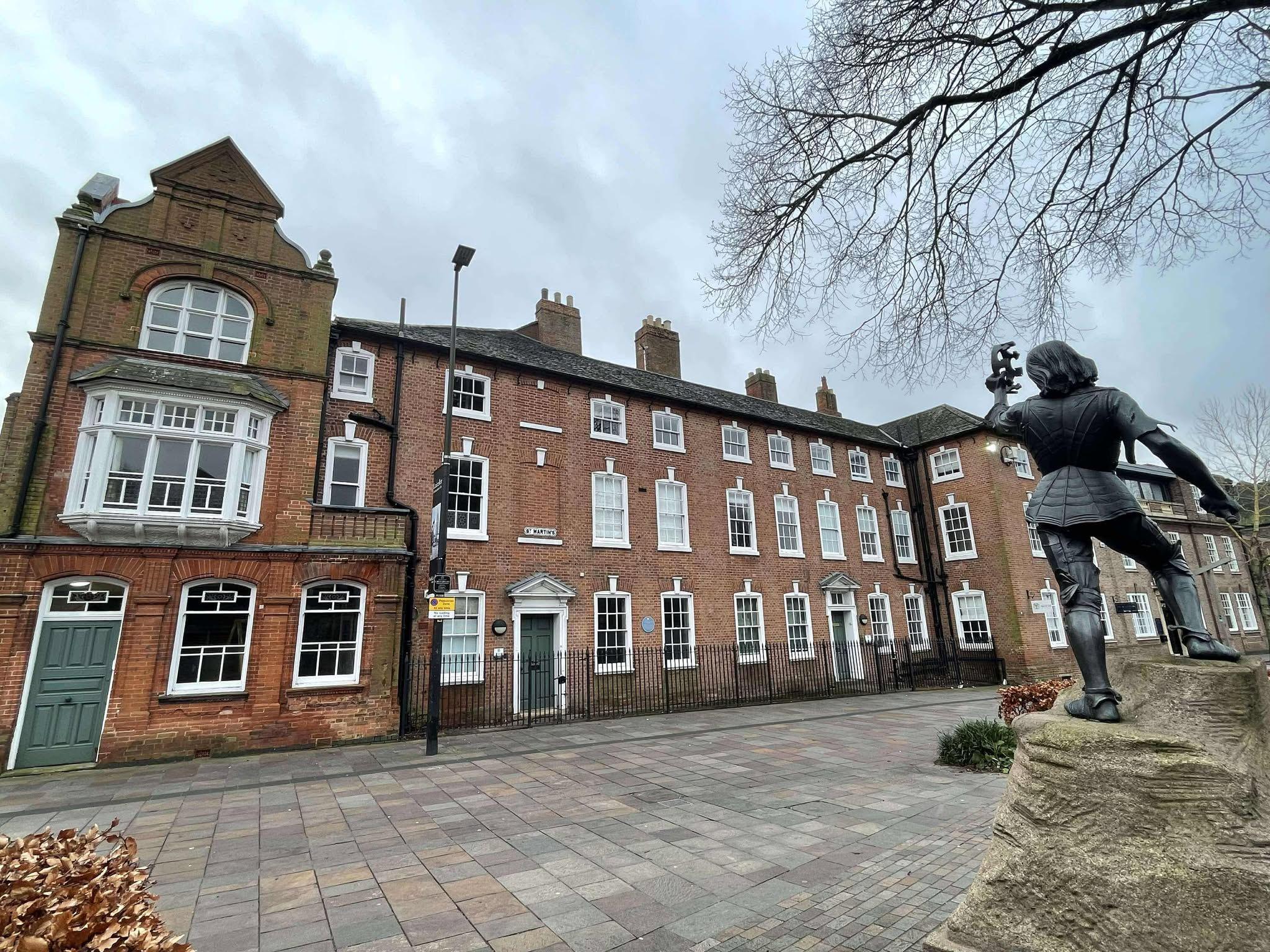 A terrace of red brick buildings facing towards a statue of King Richard III holding a crown aloft