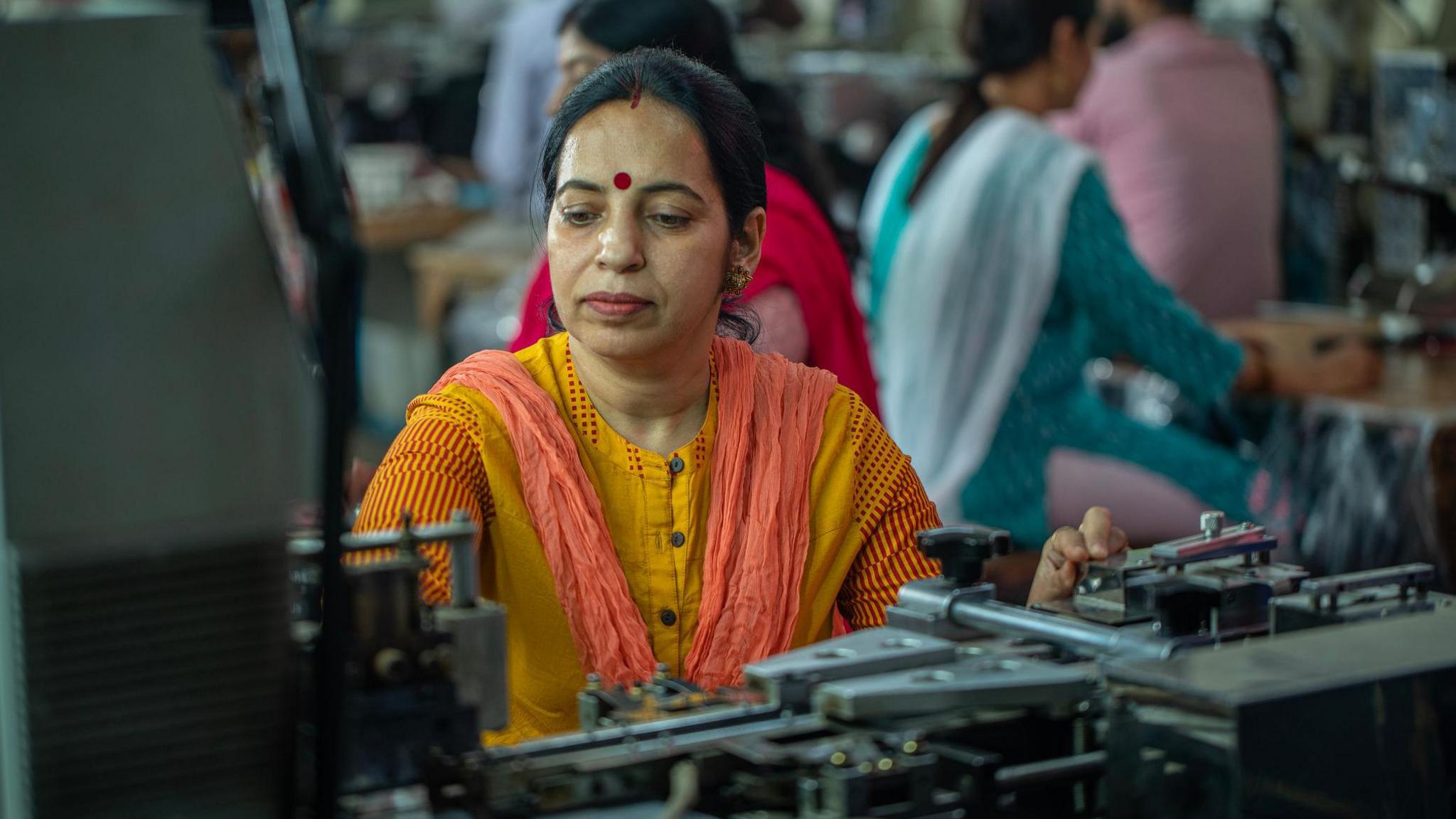 Indian female workers wearing traditional dresses using fabric printing and cutting machineries at textile factory representing women empowerment