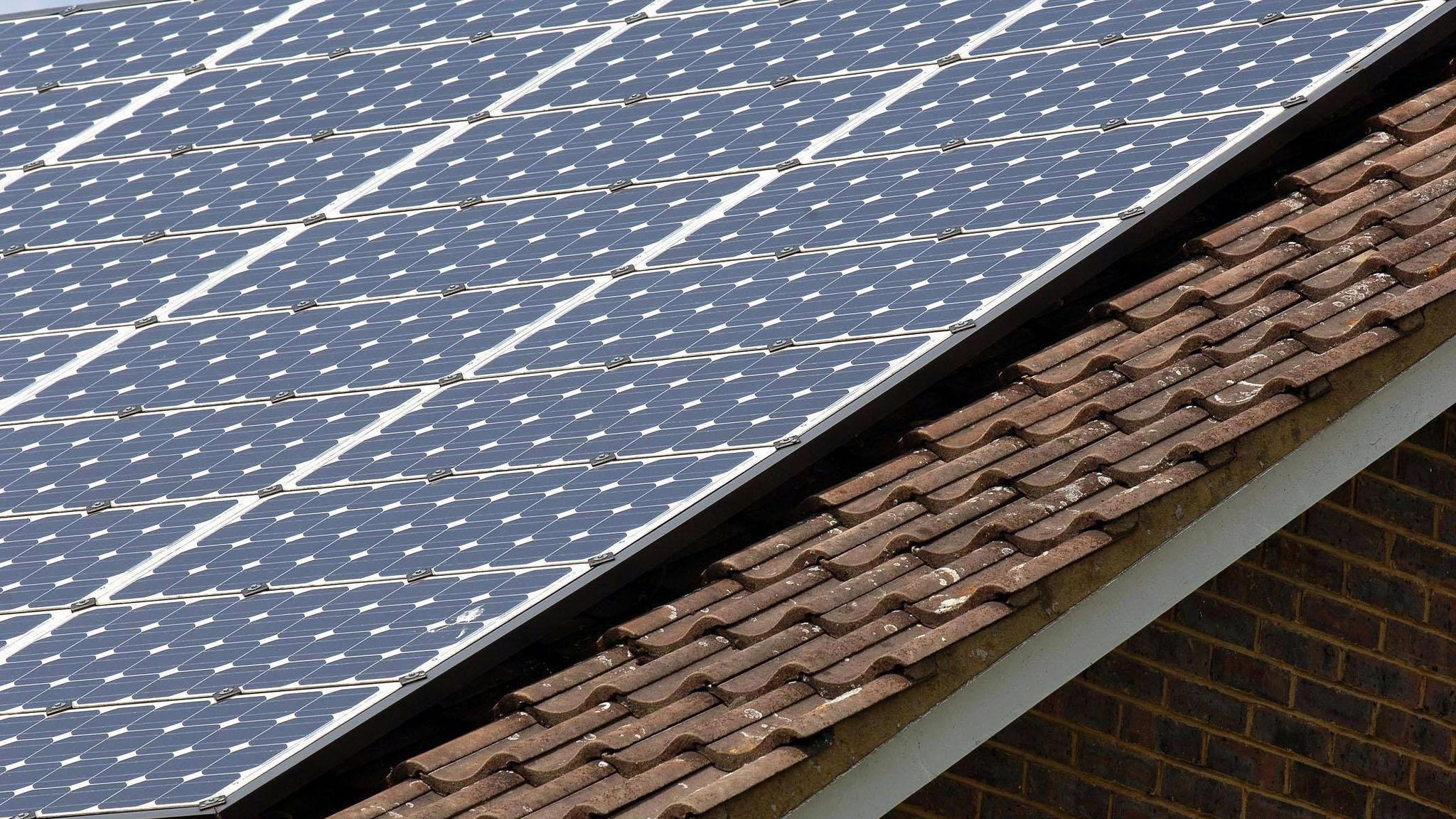 Close-up of a sloped house roof fitted with rows of blue solar panels mounted above brown tiled roofing.