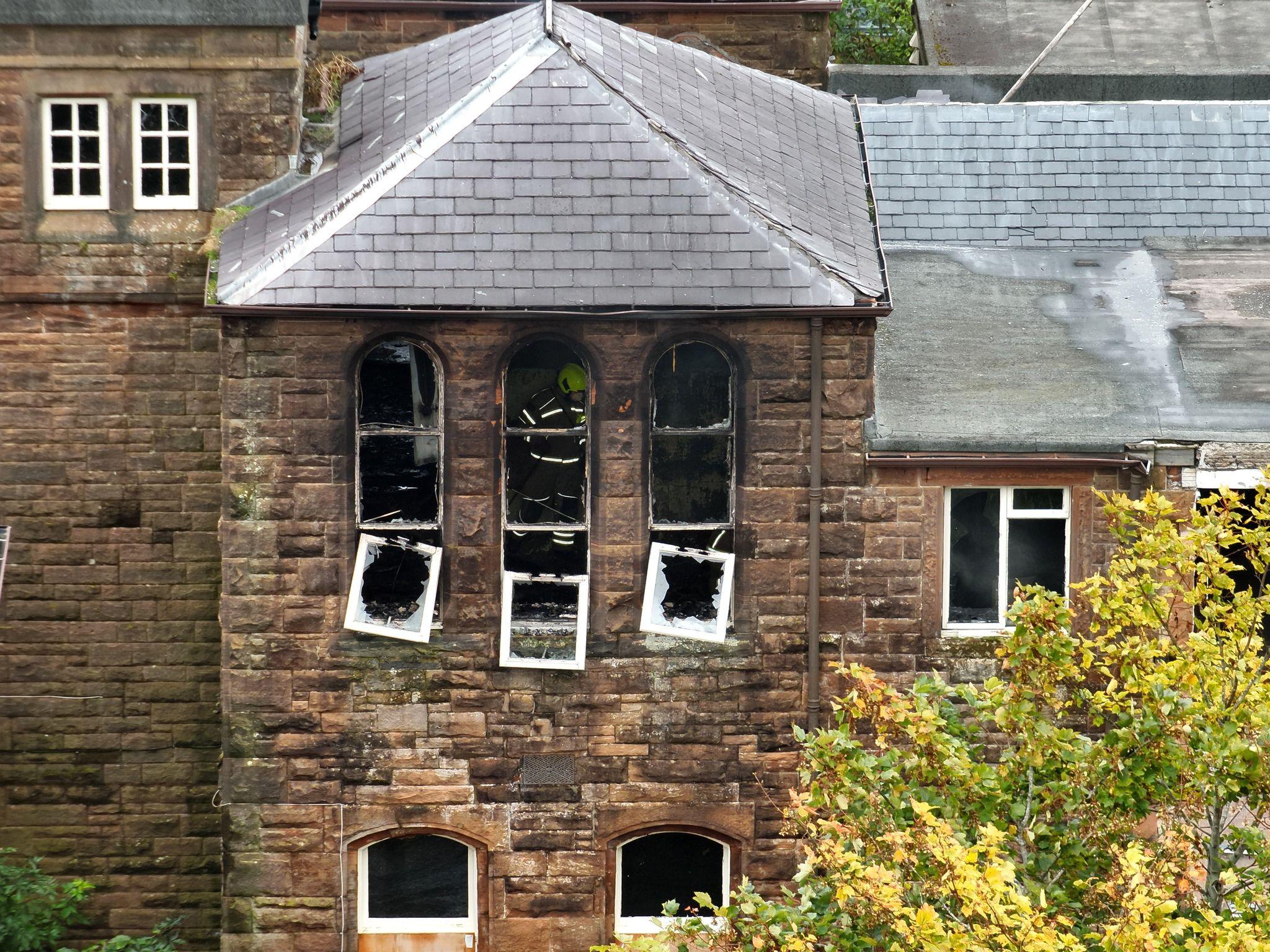 The same hospital building from a different angle with burned-out windows and a member of the fire crew visible through one window.