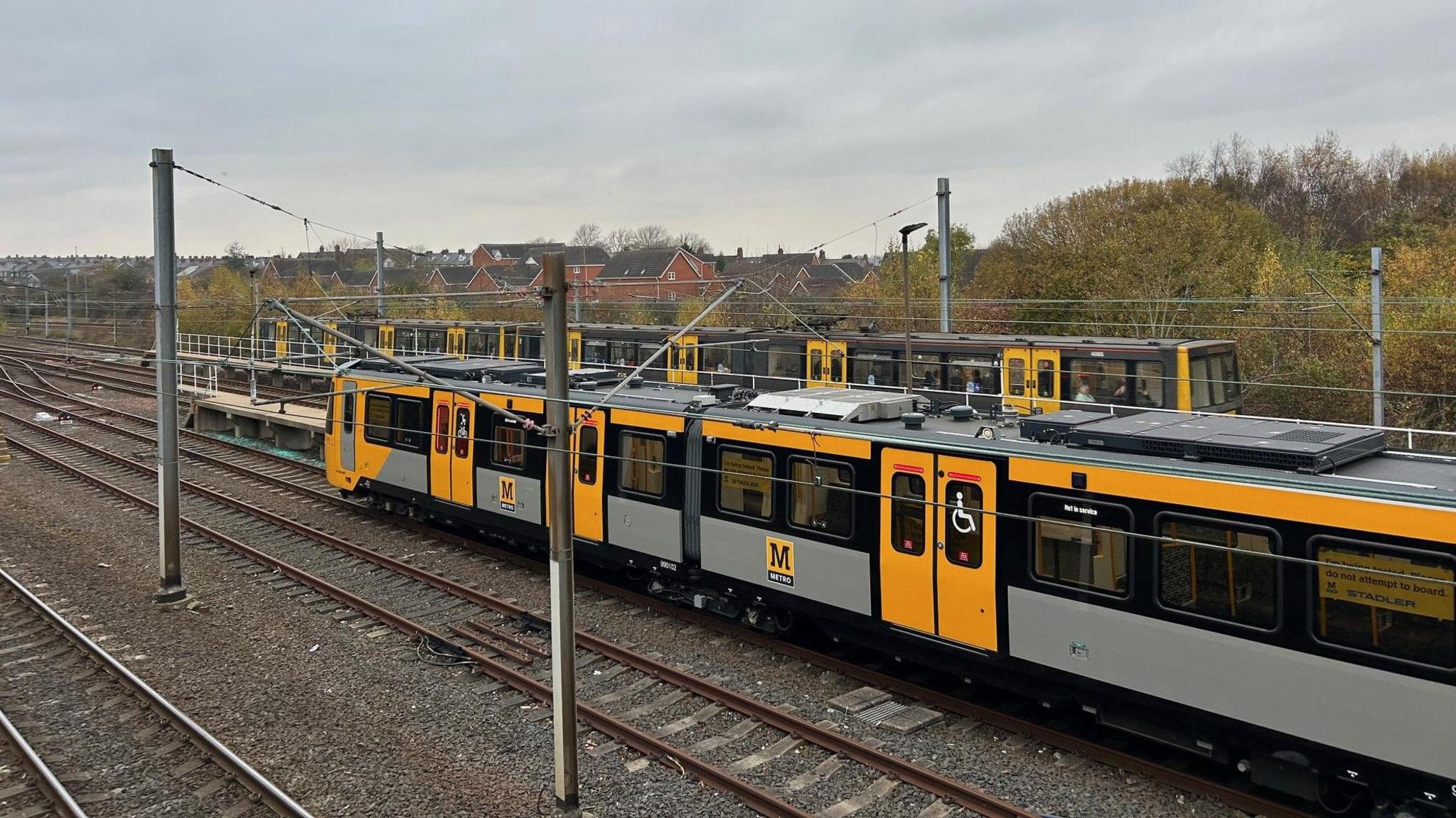 A new Metro waiting on the tracks at Pelaw. An existing Metro carrying passengers moves past it.