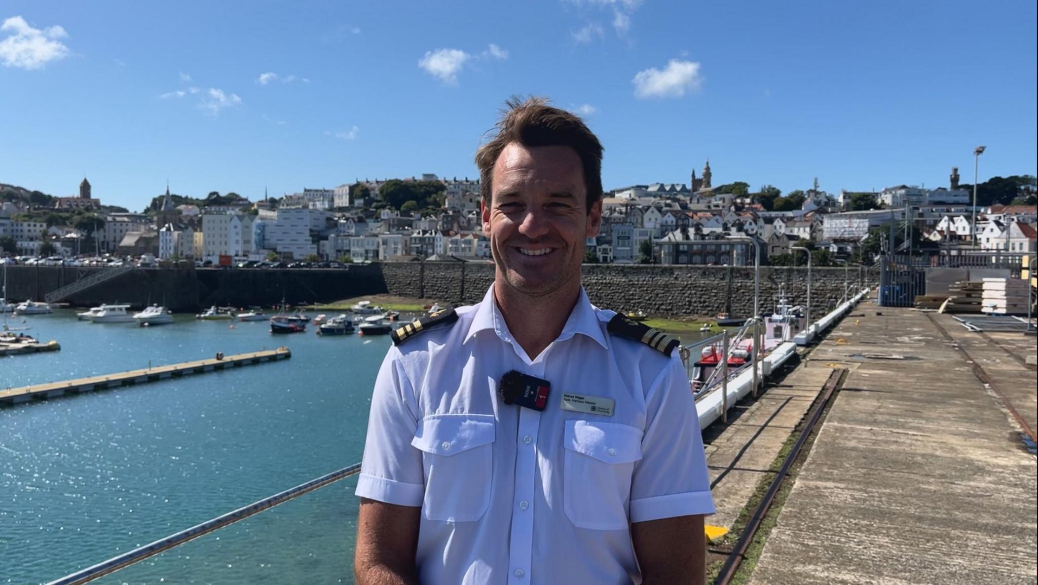 A picture of the Assistant Harbour Master, Kieran Higgs in uniform stood in front of St Peter Port Harbour.