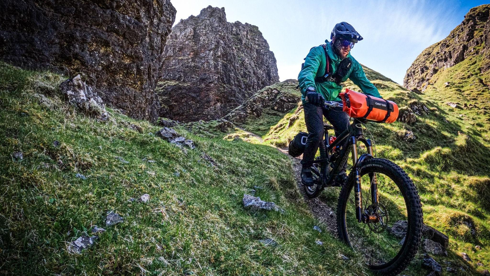 A person on a mountain bike, wearing a black helmet and a green jacket, rides down a grassy hill.