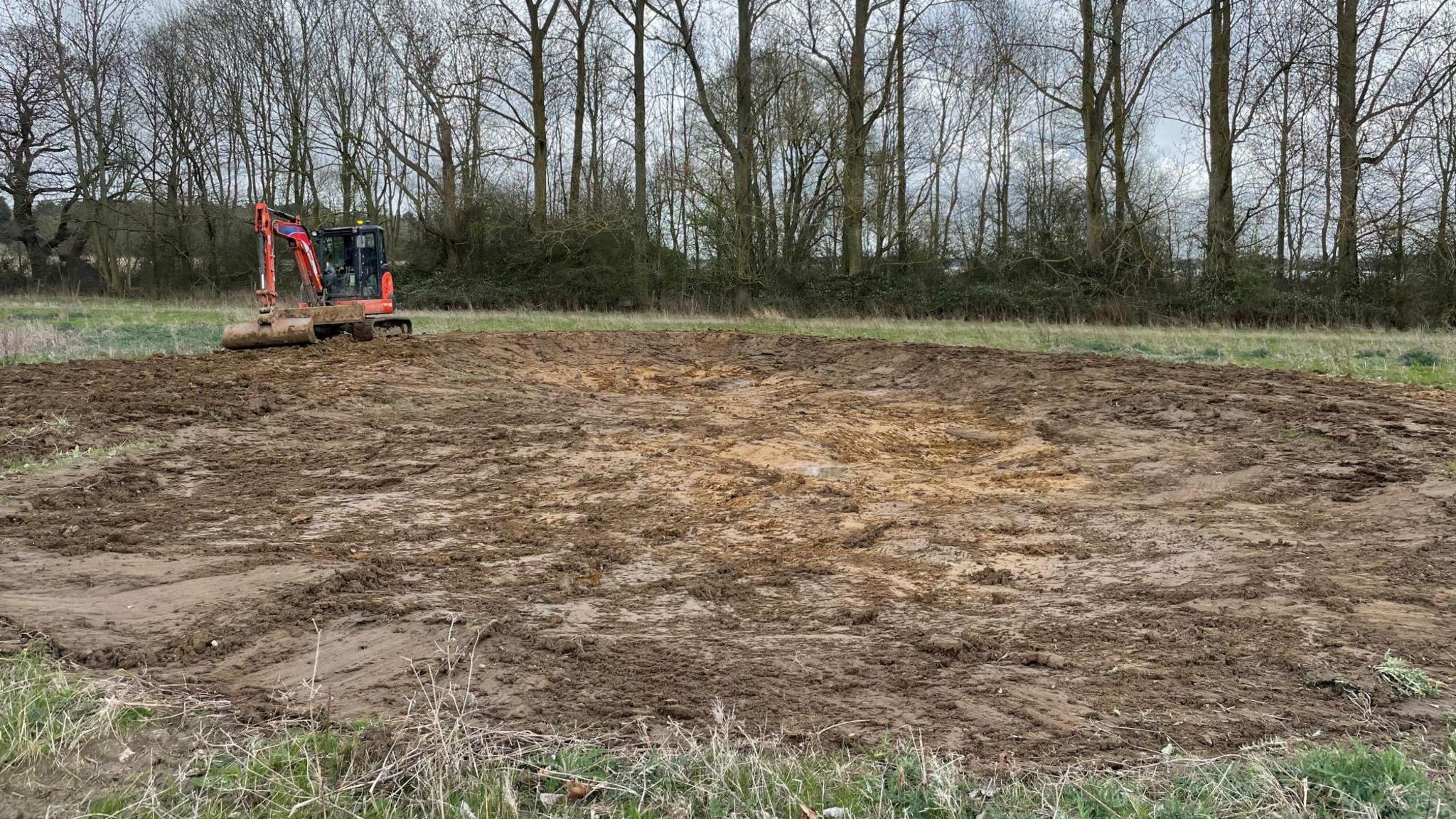 A person uses a digger to create the pond