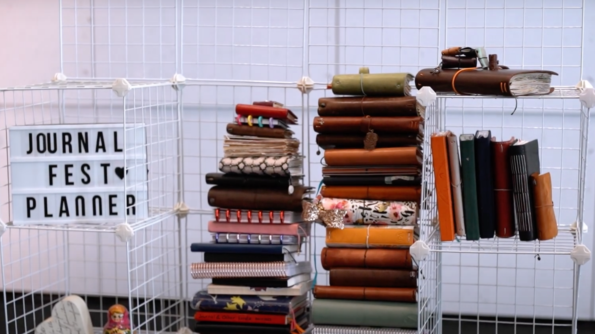 White crates are stacked on top of one another. A pile of brown and tan coloured leather books are sitting inside the crates.