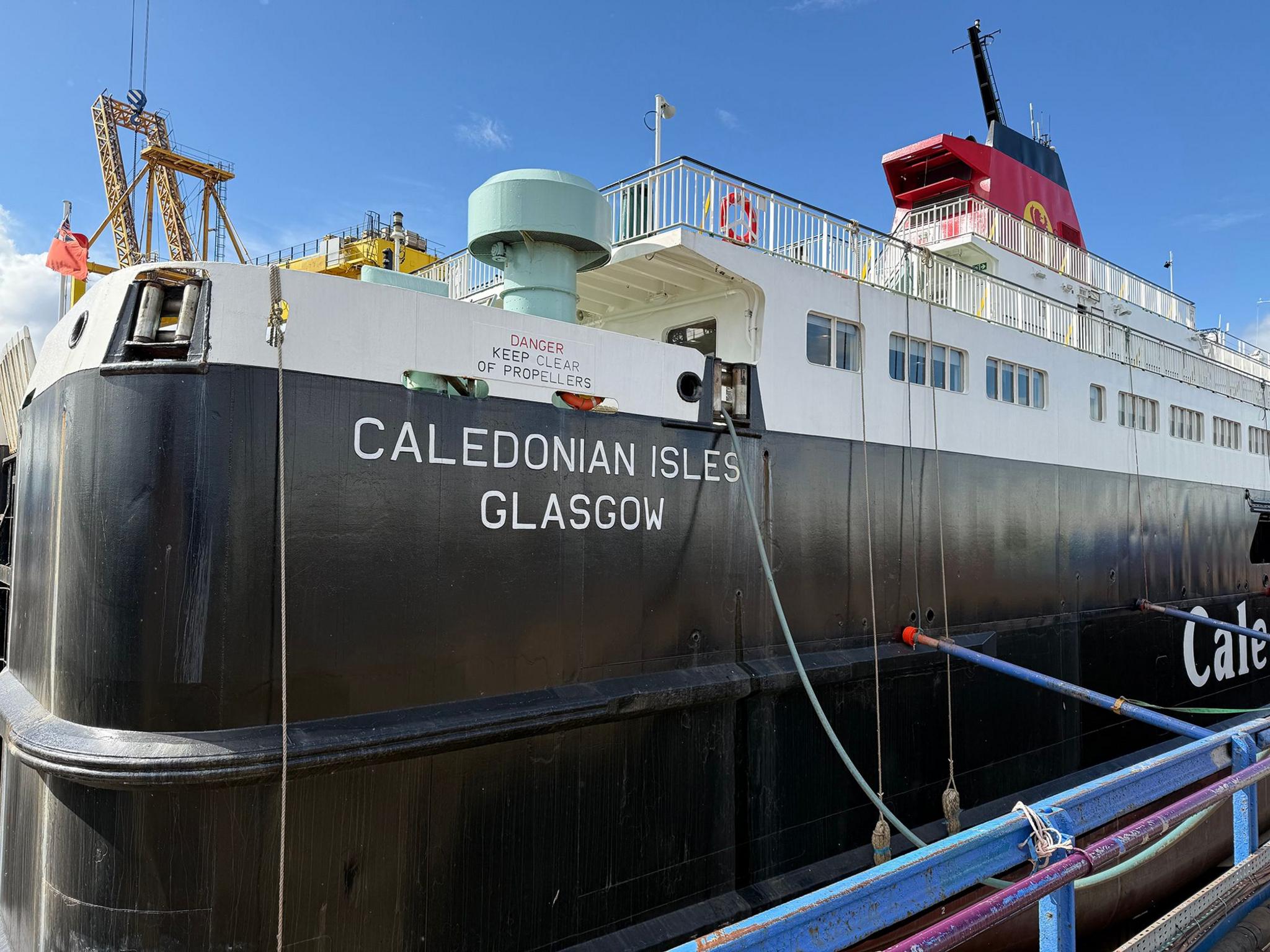 The rear of a large black and white ferry with a red funnel. The name Caledonian Isles can be seen on the ship's side. 