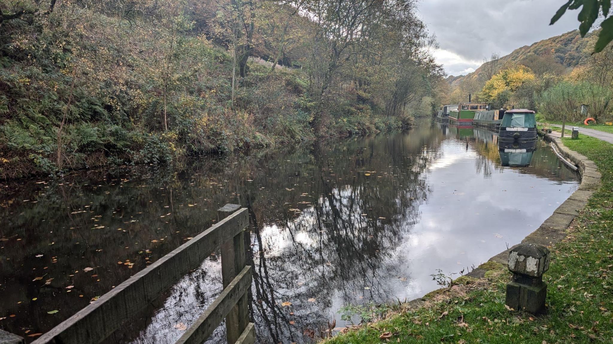 A picture of a river surrounded by hills and trees with several barges moored on the riverside. 