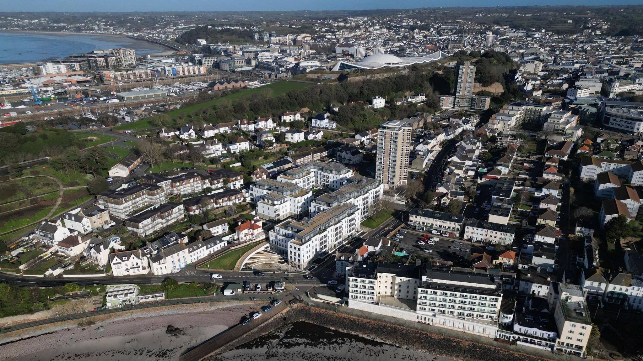 An aerial view over St Helier. There are high rises and buildings stretching in to the distance. A bay can be seen to the far left.