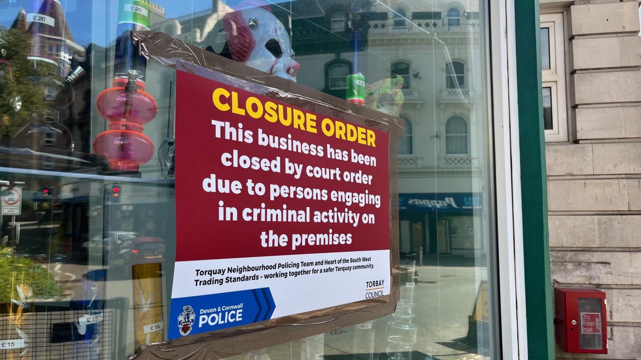 A sign on a shop window reads: Closure Order. This business has been closed by court order due to persons engaging in criminal activity on the premises.