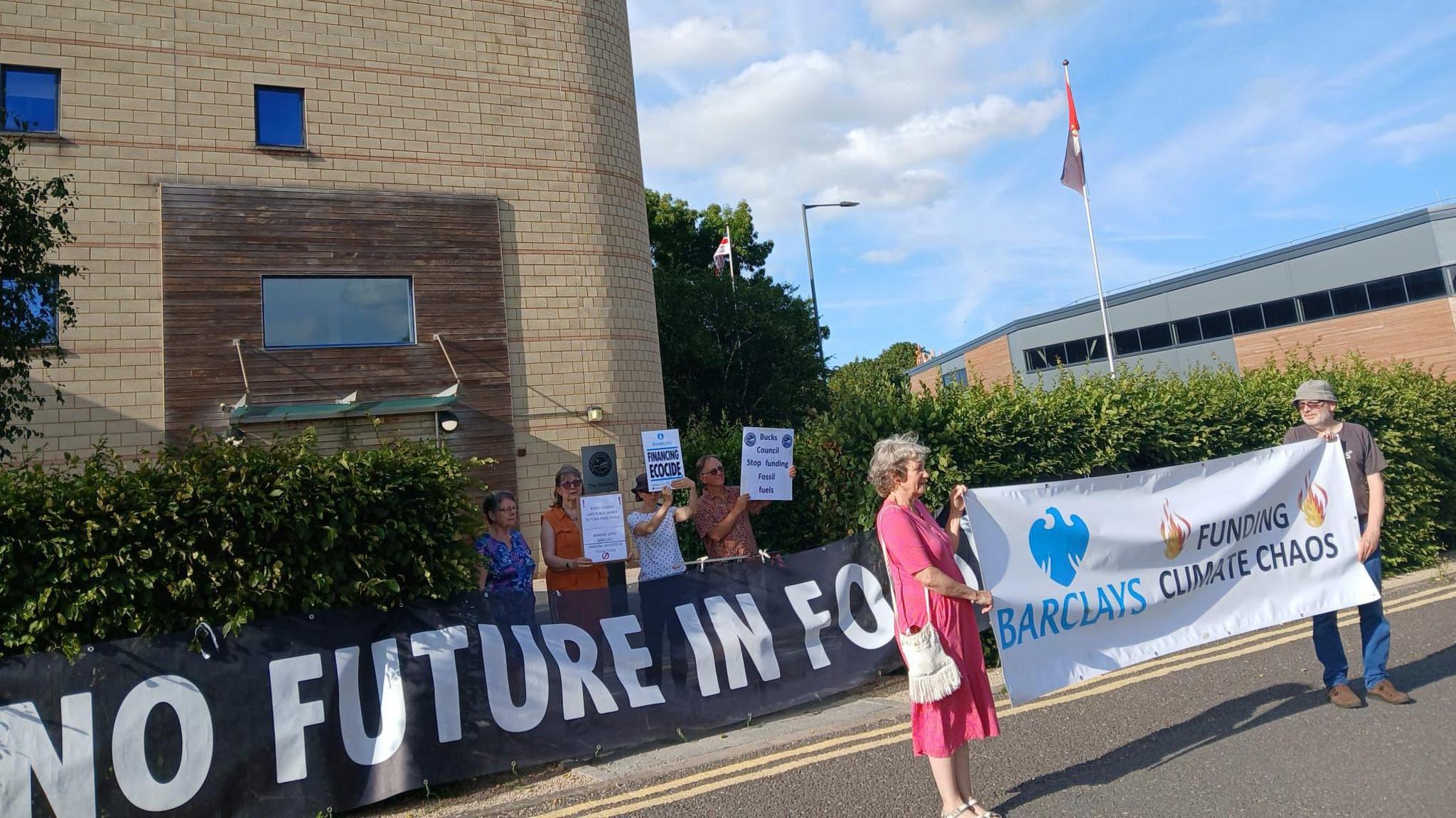 A group from 'Bucks Council Stop Funding Fossil Fuels' hold banners outside Buckinghamshire Council offices on a sunny Sunday in June 2025.