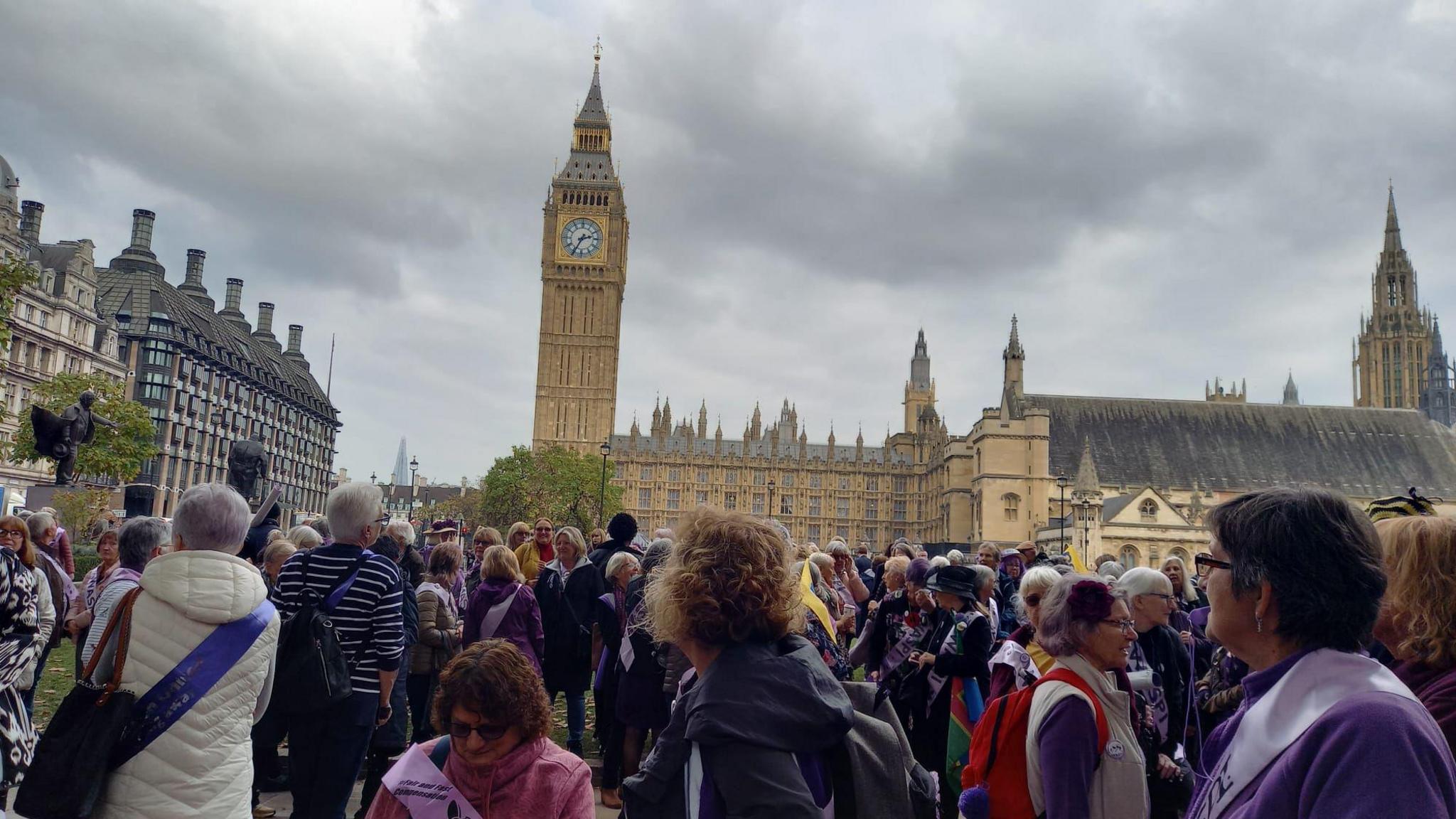 A group of people gathered in Parliament Square. The Houses of Parliament and Elizabeth Tower are in the background. 