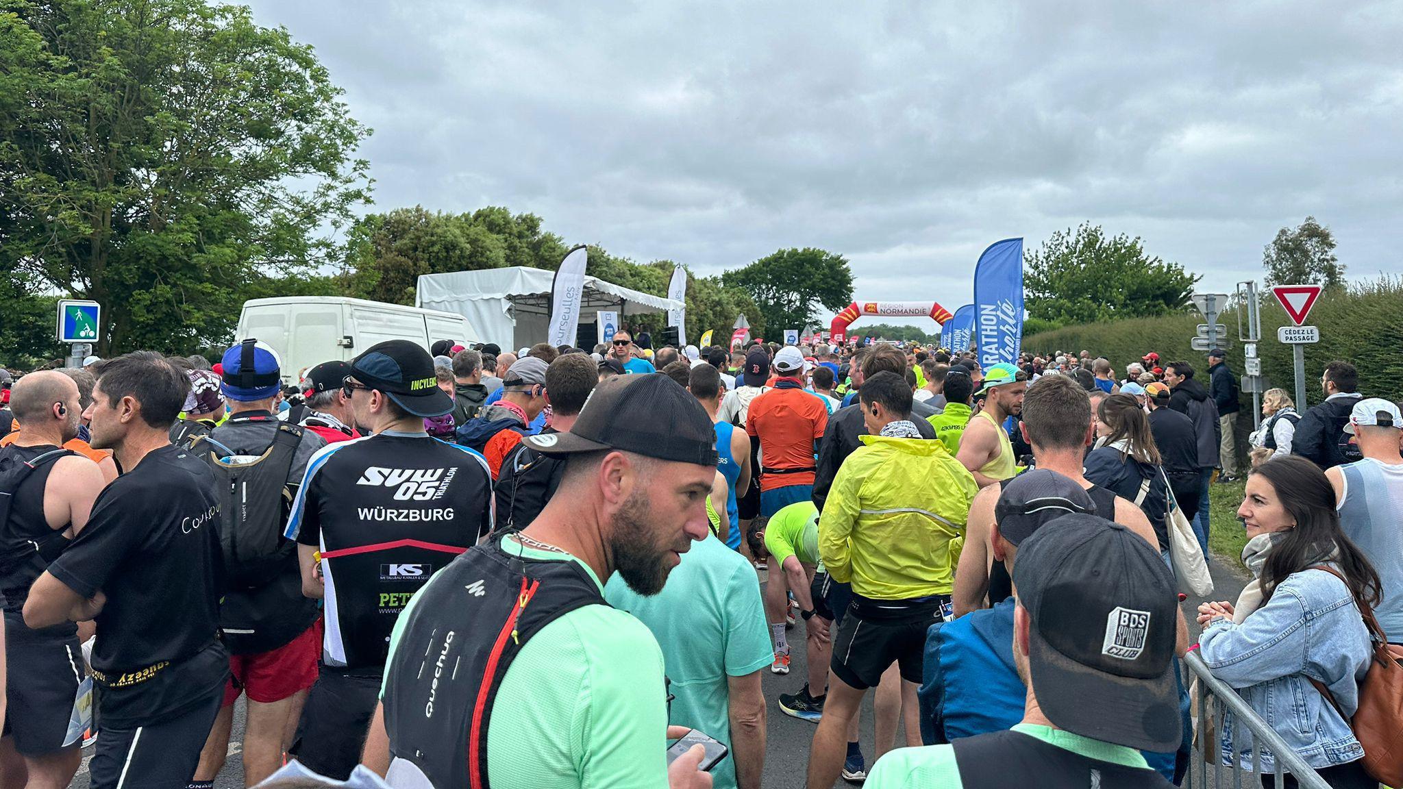 A large group of runners stand waiting to start the race with the start line in the distance