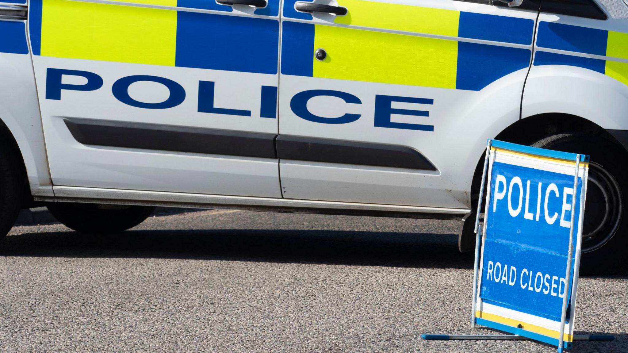 A police van parks next to a "police road closed" sign.