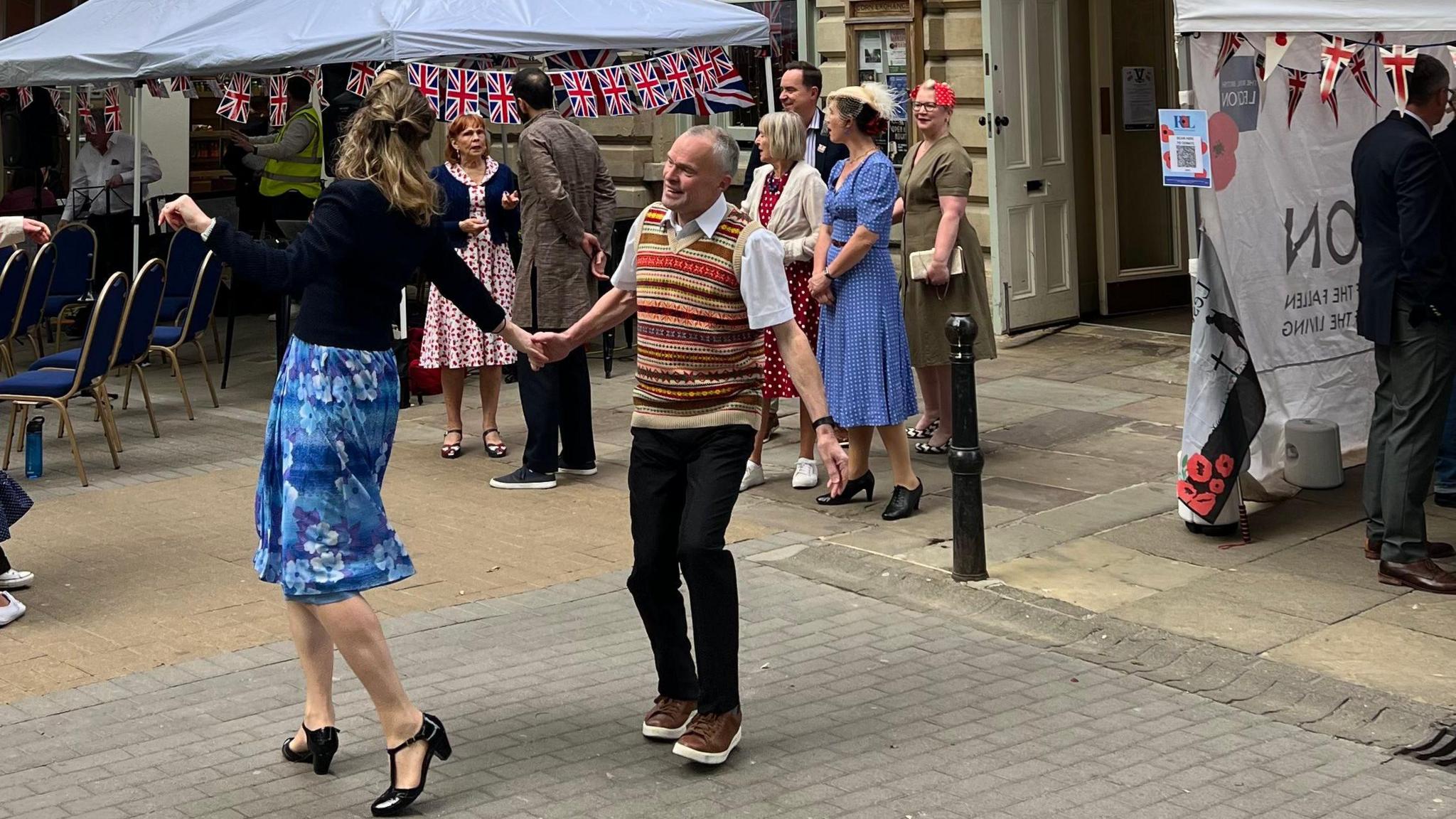 A man and woman dancing in the street as others stand and watch.