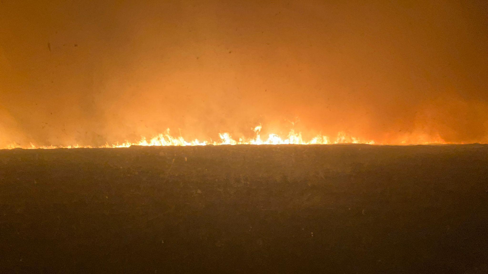This is a picture of the view from 'Water Guy' Chris Lord's vehicle as he helped fight the Langdale Moor fire. The flames are really close to the cab and spread from one side of the image to the other. The sky is a mixture of black and orange.