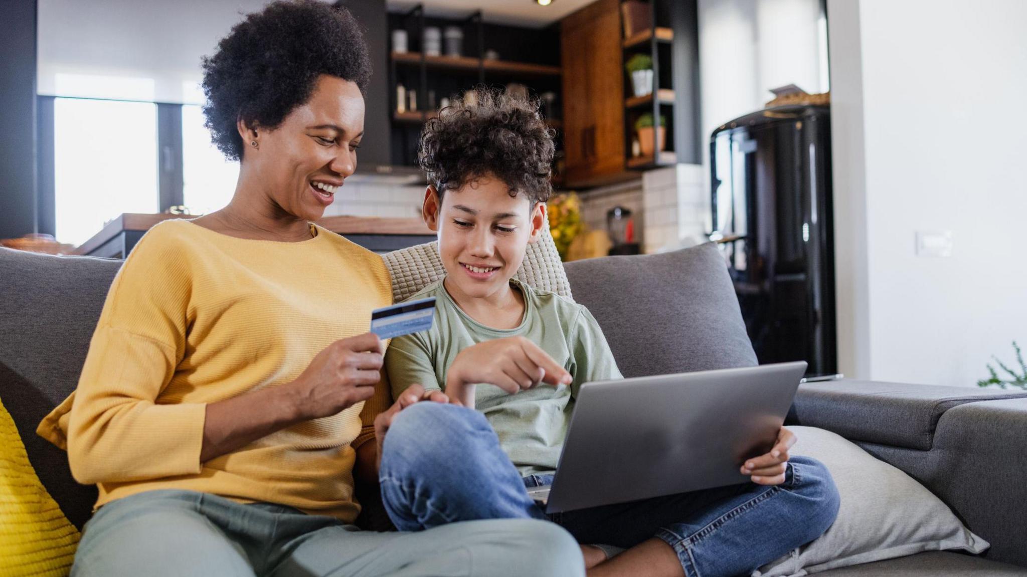 mother helping son to understand online banking sat on the sofa at home.