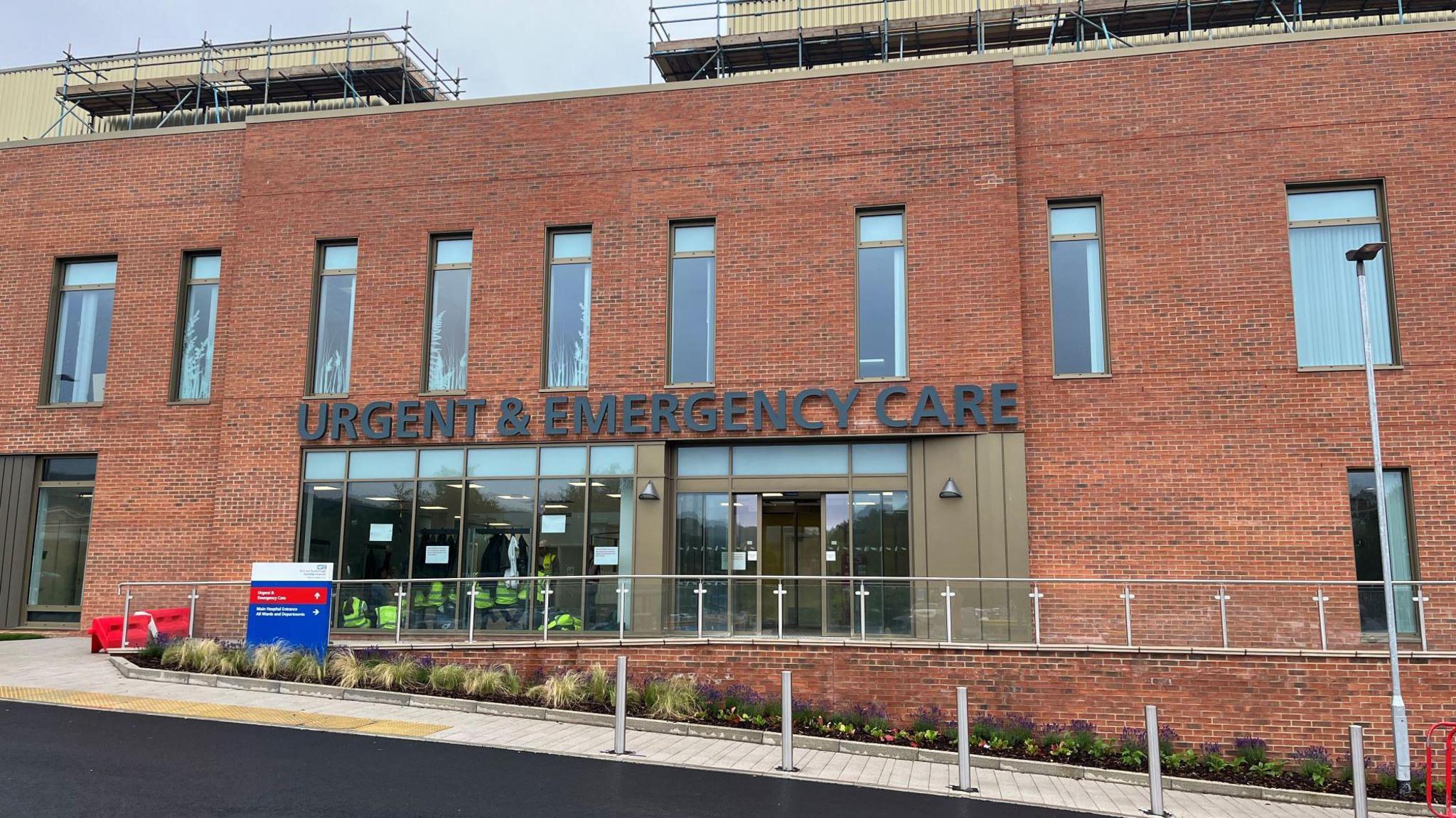 New-build red-brick building with a sign reading "Urgent and Emergency Care" above the entrance.