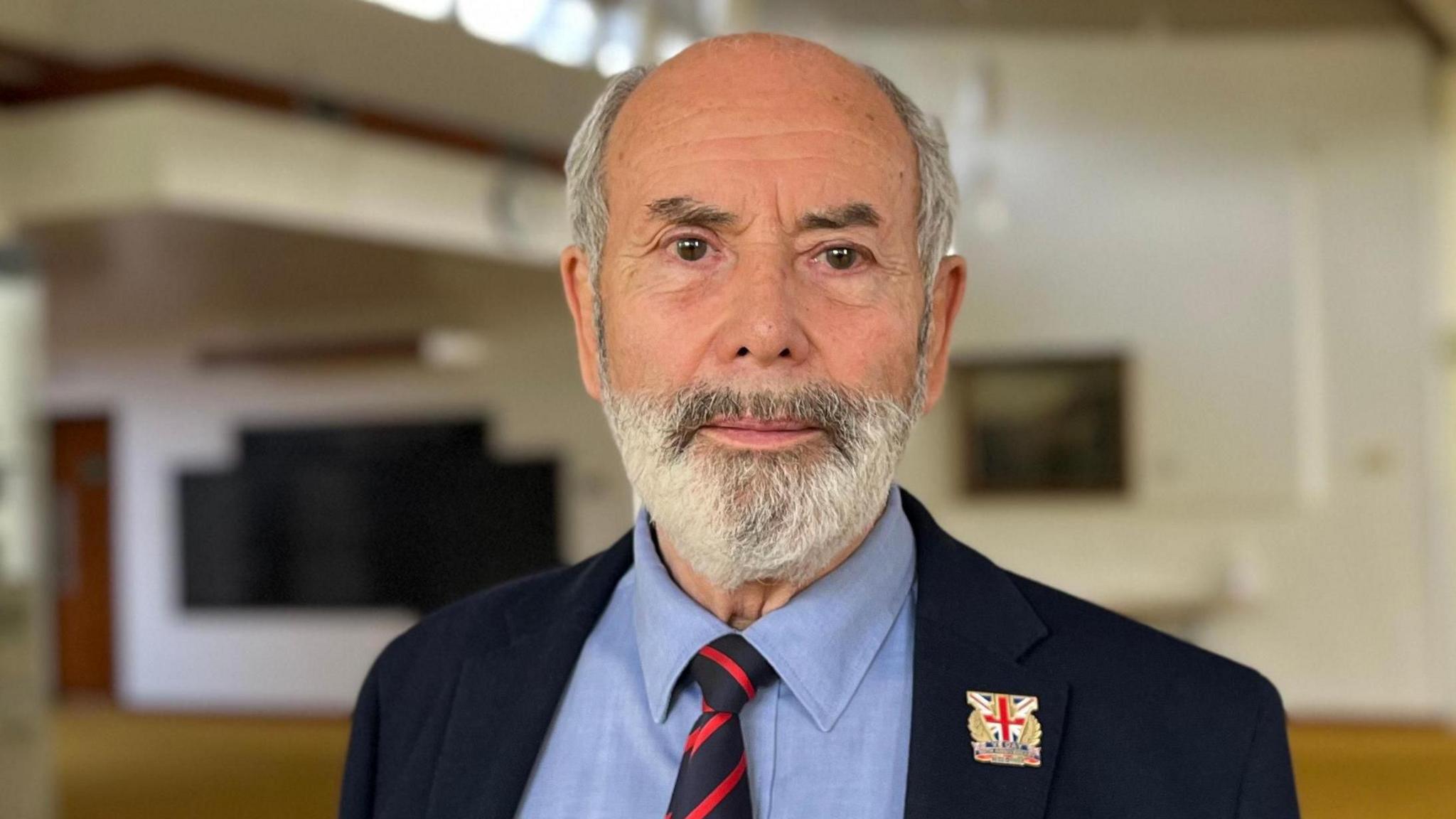 A man with a beard in a blue suit. He wears a union flag badge