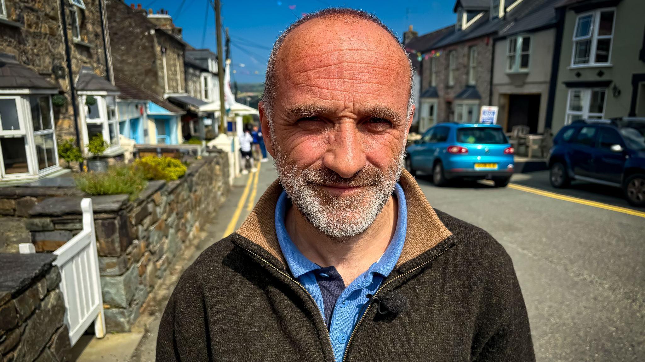 Hedd Ladd Lewis standing on a pavement in Newport with stone terraced homes in the background, including one with a for sale sign