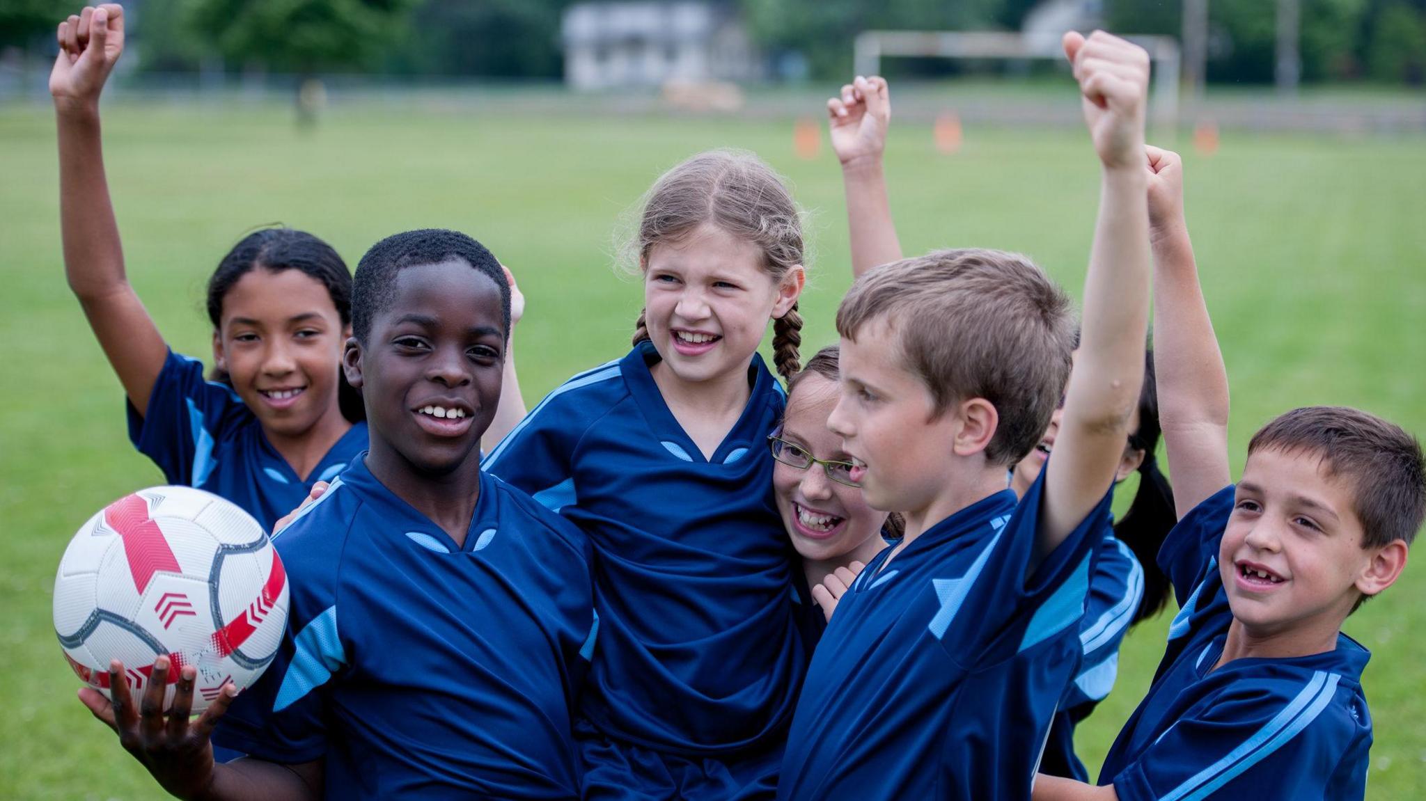 children in PE kit with football.