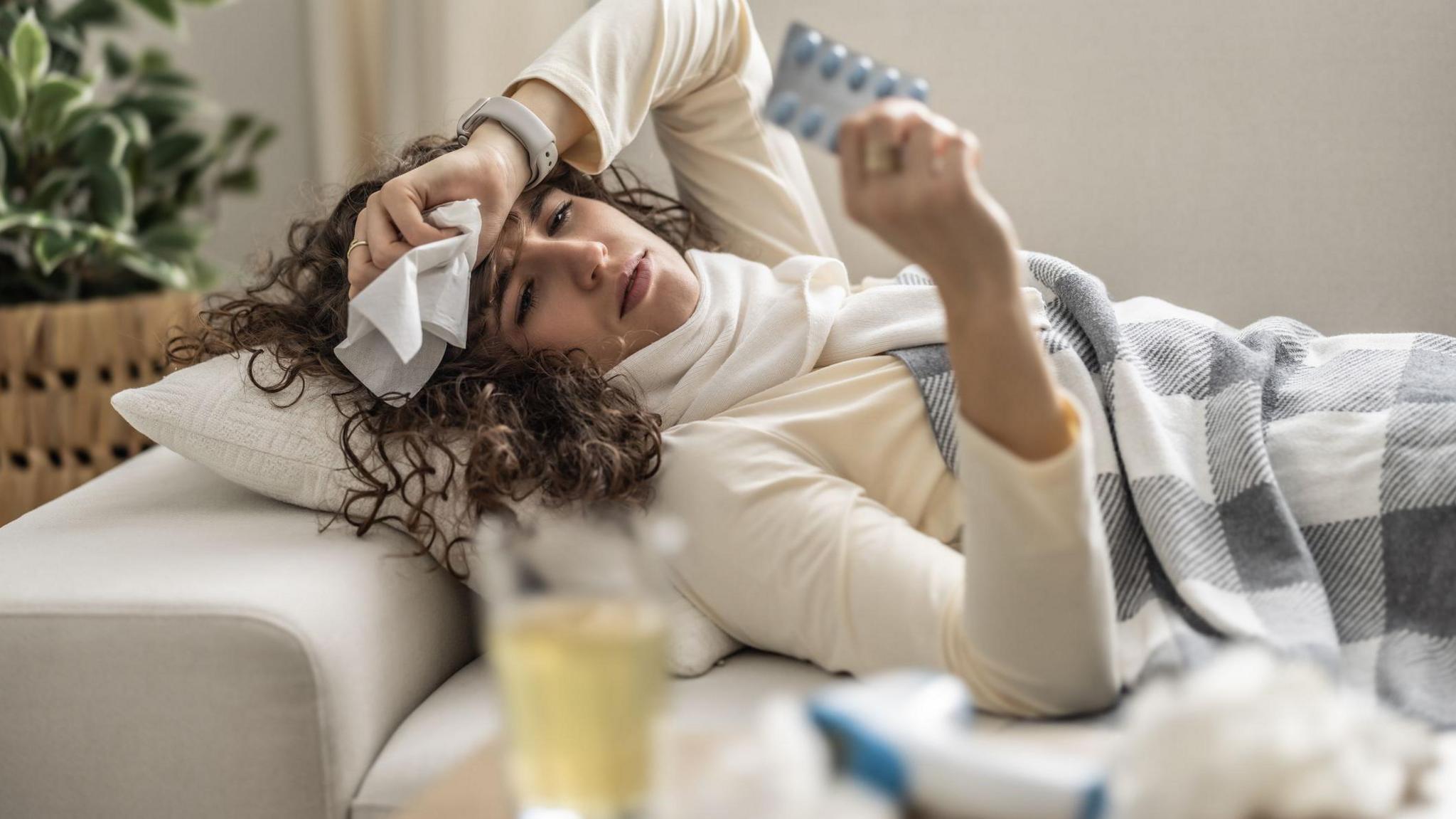 Sick young woman lying on the couch holding a blister pack with antibiotics. 