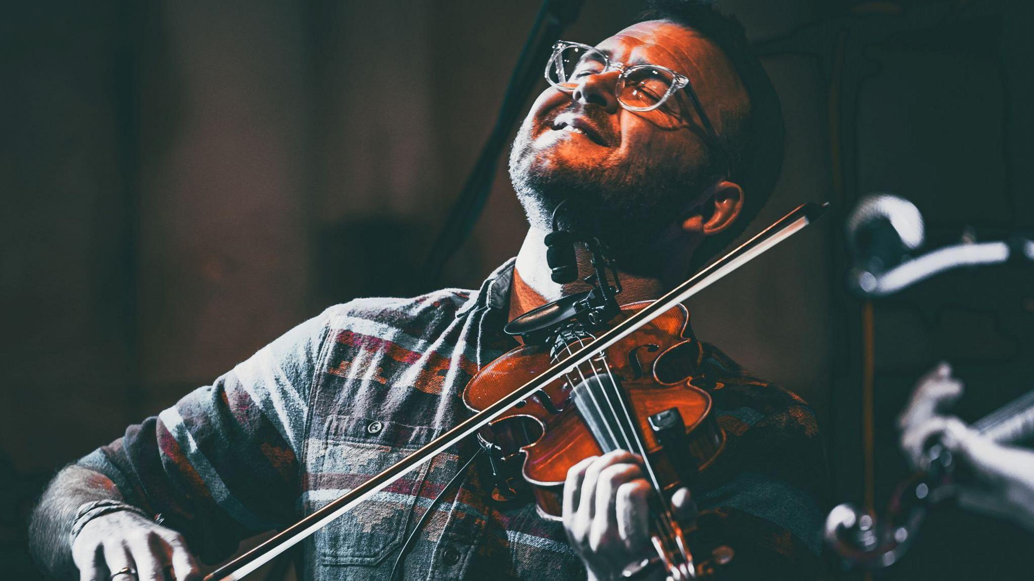 Headliner Sam Sweeny with a violin and his eyes closed playing music.