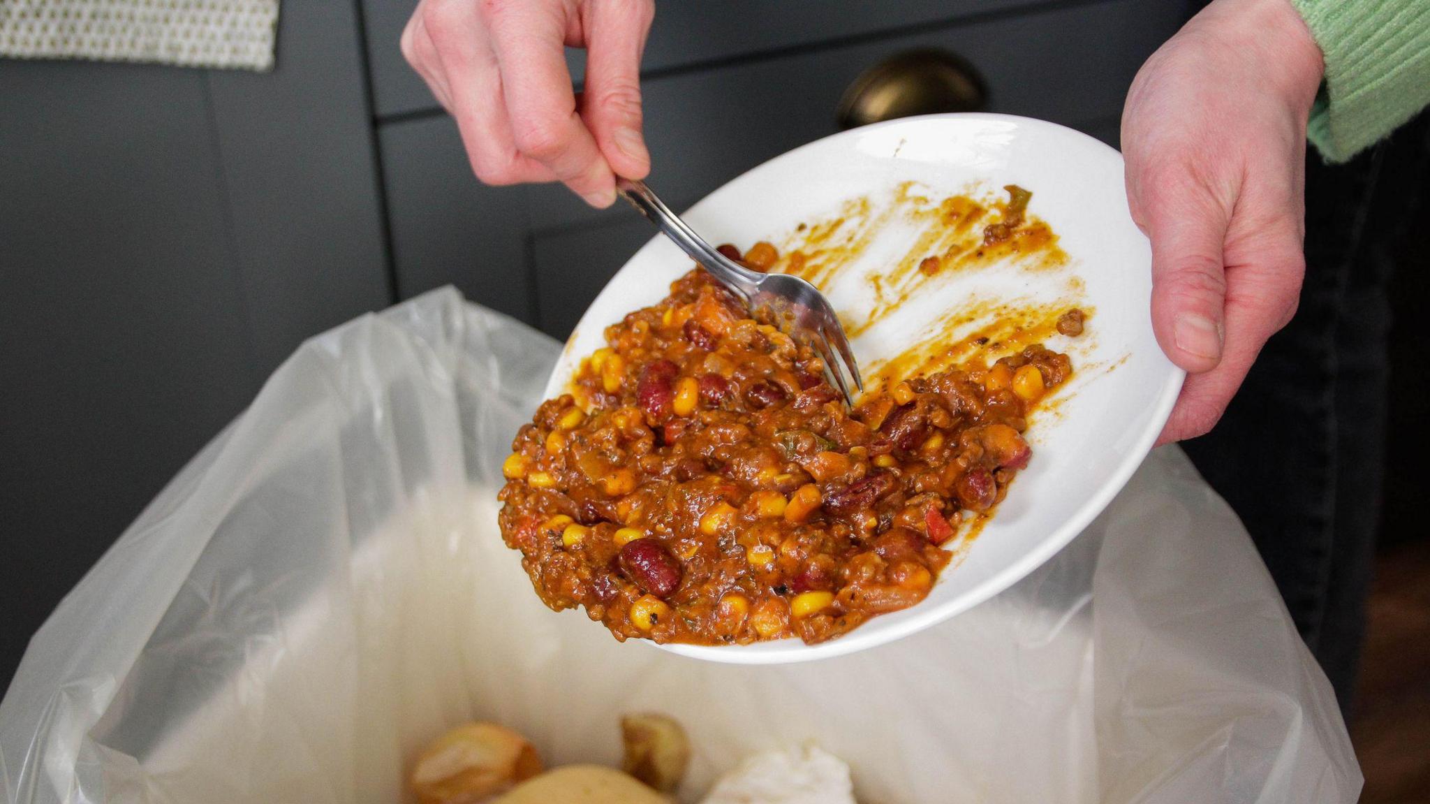 Woman scraping leftover curry off a plate into a bin