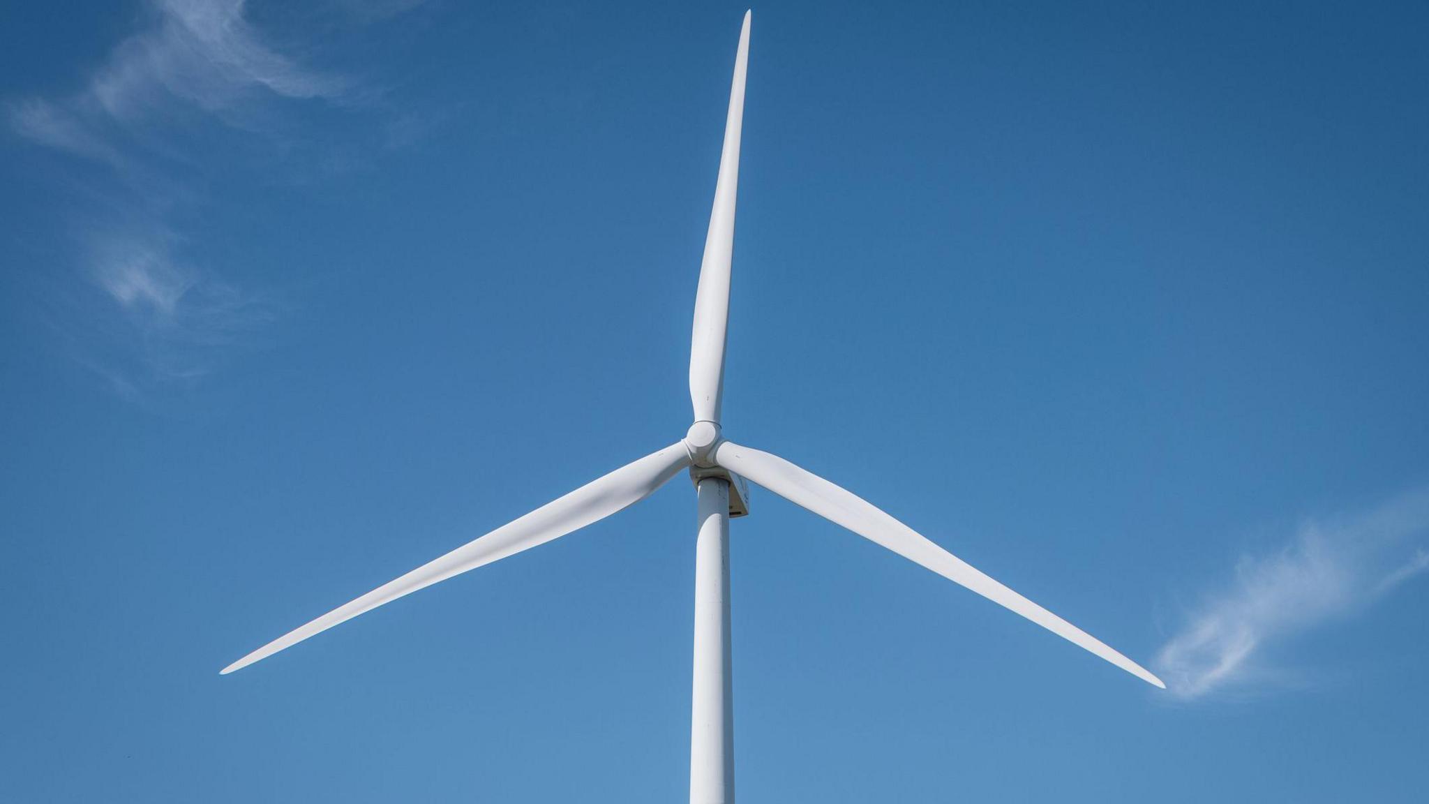 A single white wind turbine against an almost cloudless blue sky