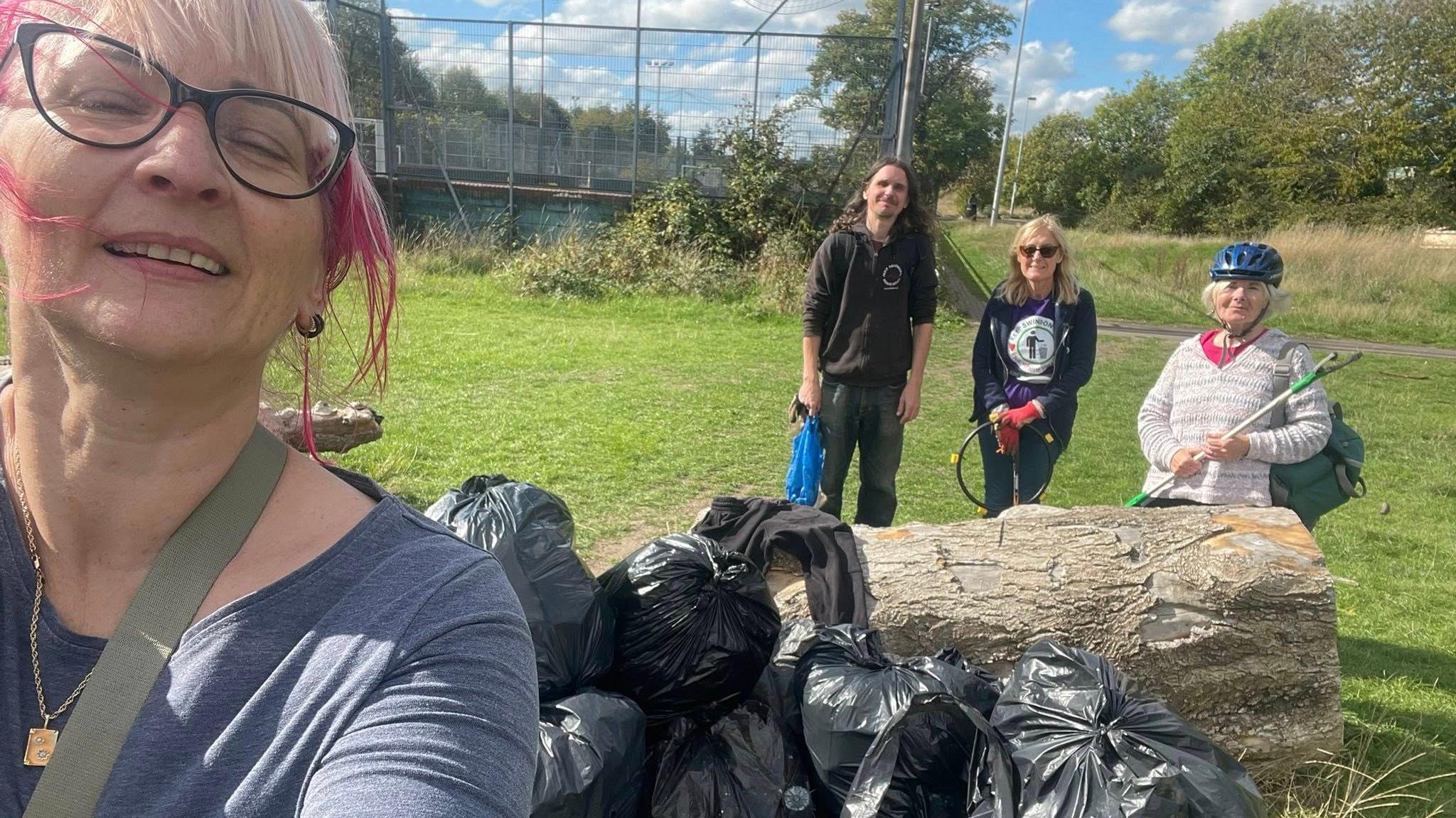 Keep Swindon Tidy volunteers smile at a camera with piles of bin bags and football pitches in the background.