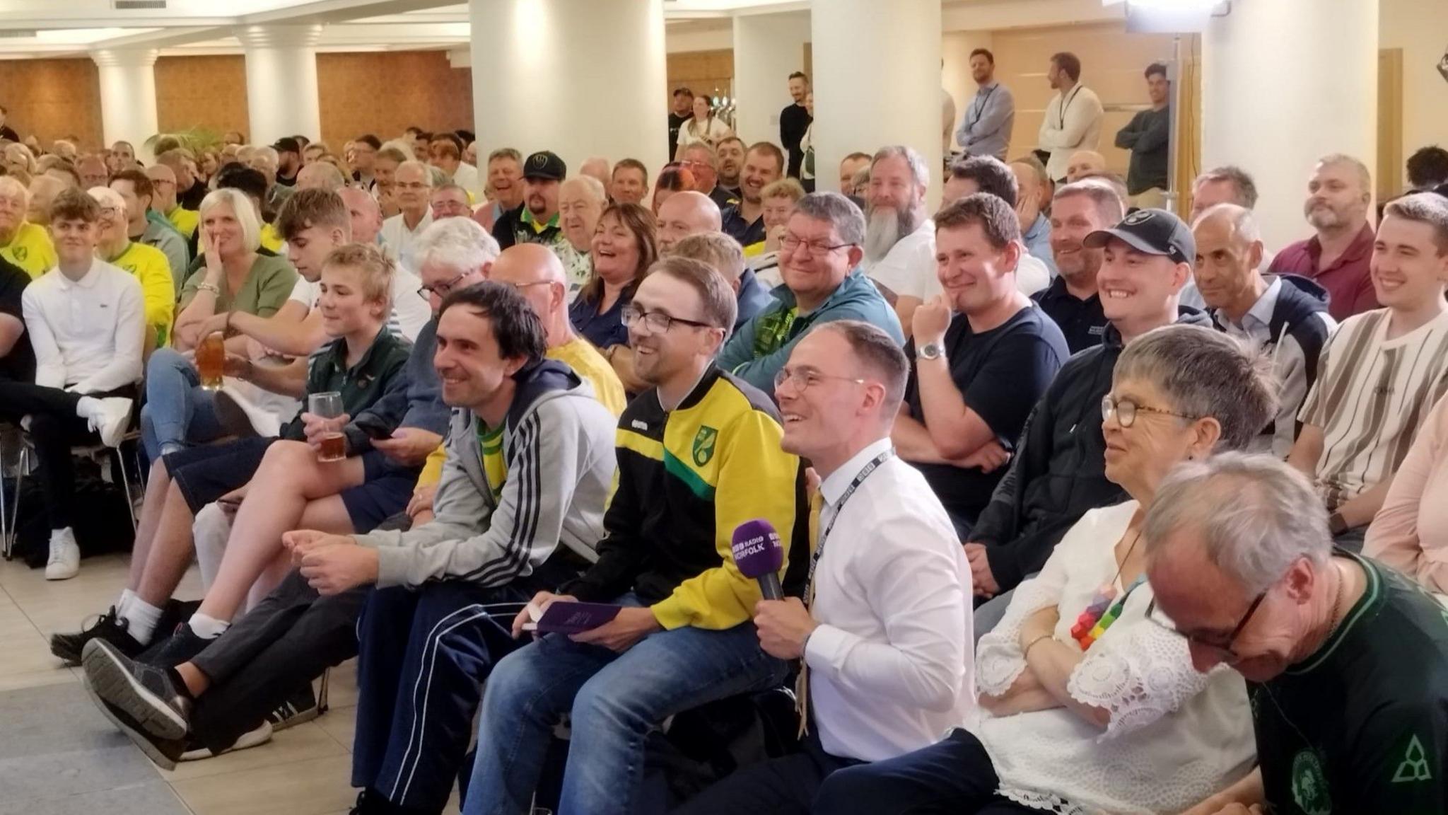 Seated people smile as they listen to speakers addressing their questions in a room.