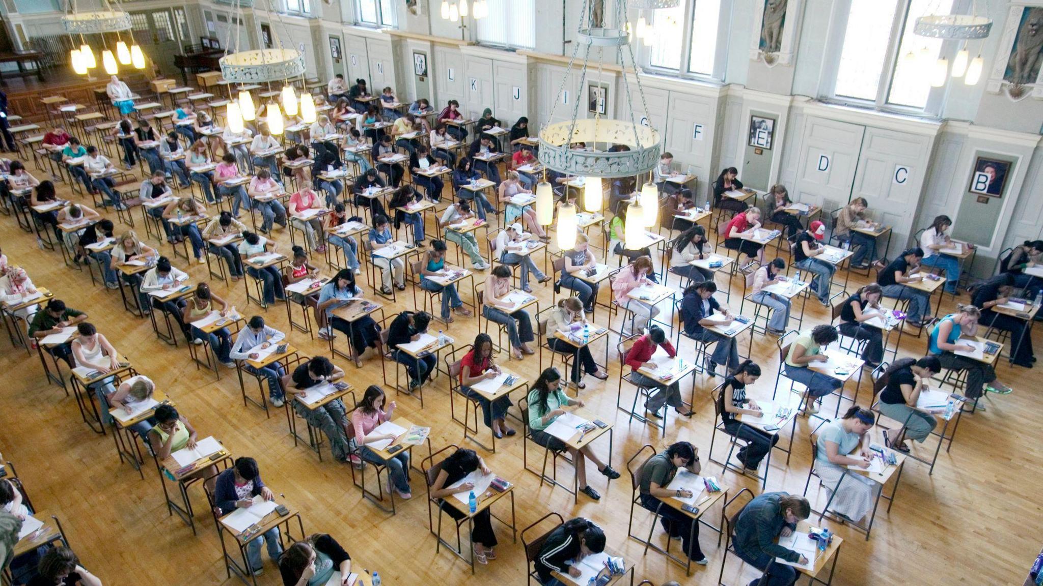 A photograph of students sitting exams in a school hall, all sat on individual desks