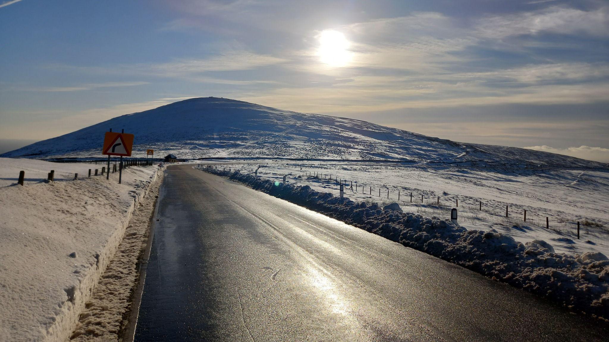 The Mountain Road cleared of snow, with snow around it and the low sun appearing above a hill in the distance.