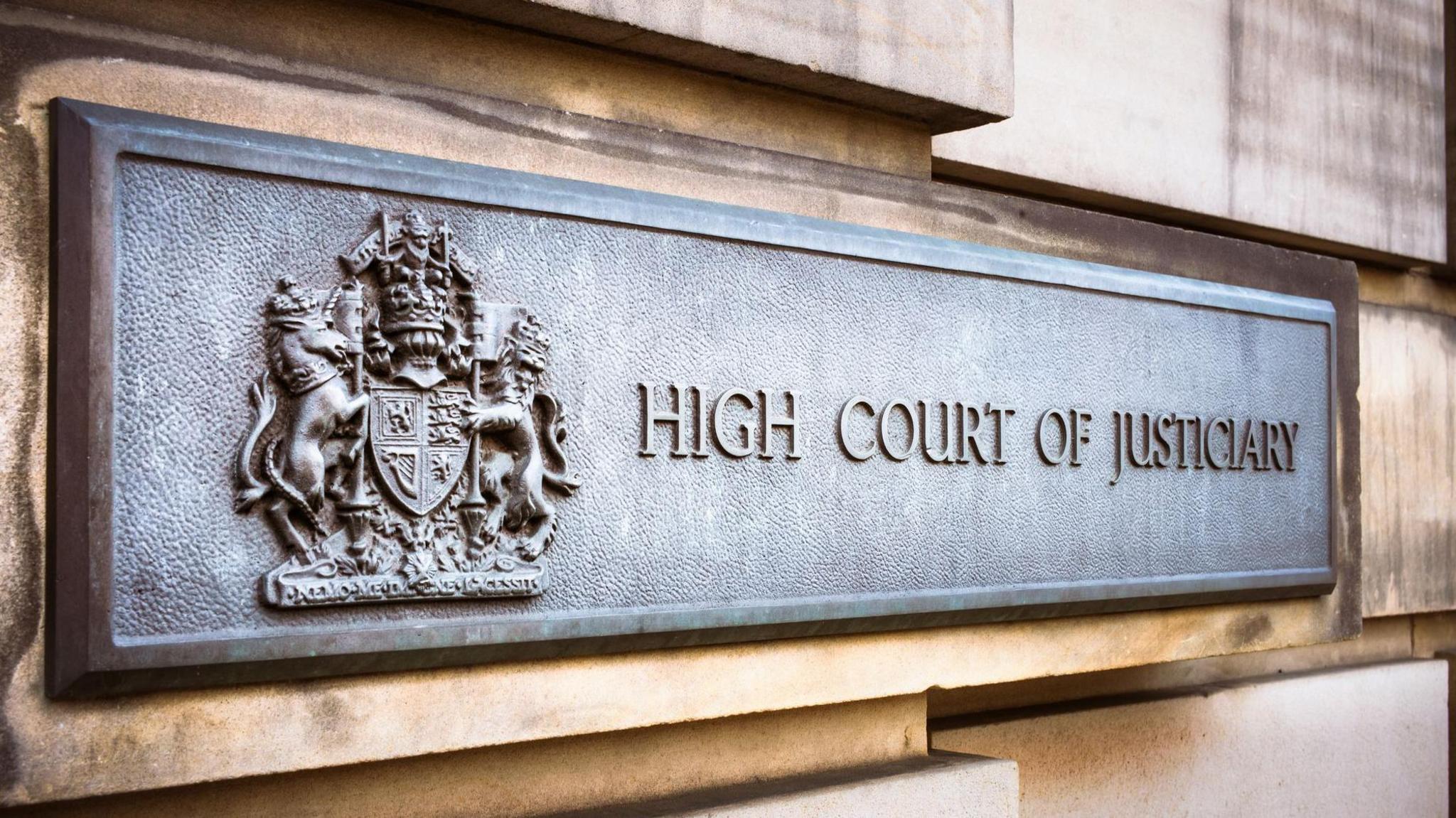 Sign on a stone exterior wall of the High Court in Edinburgh. The sign reads: "High Court of Justiciary" and includes a crest.