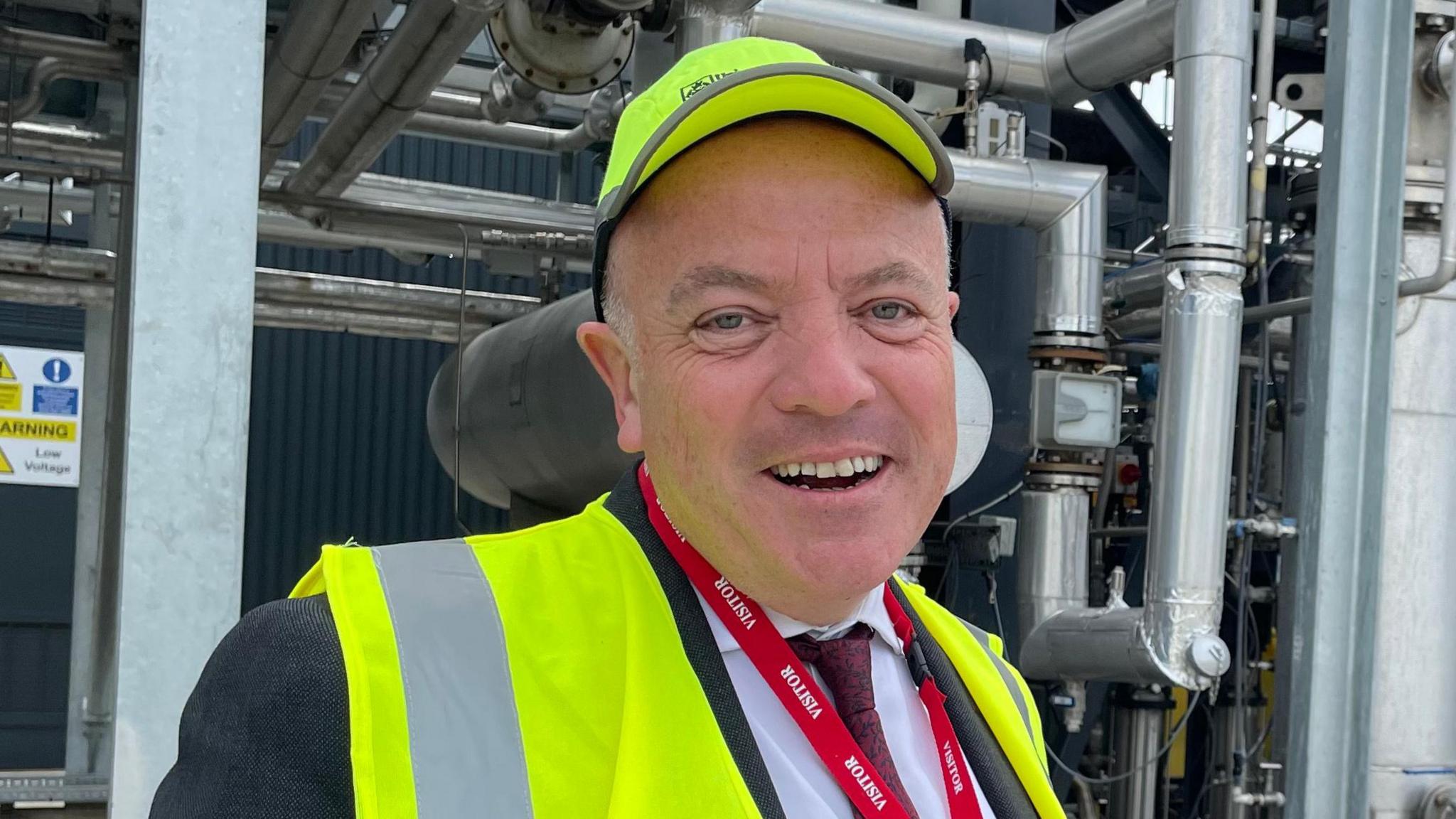 Aviation Minister Mike Kane stood in front of a network of pipes and machinery at the University of Sheffield's Advanced Manufacturing and Research Facility, wearing a high-visibility jacket and cap.