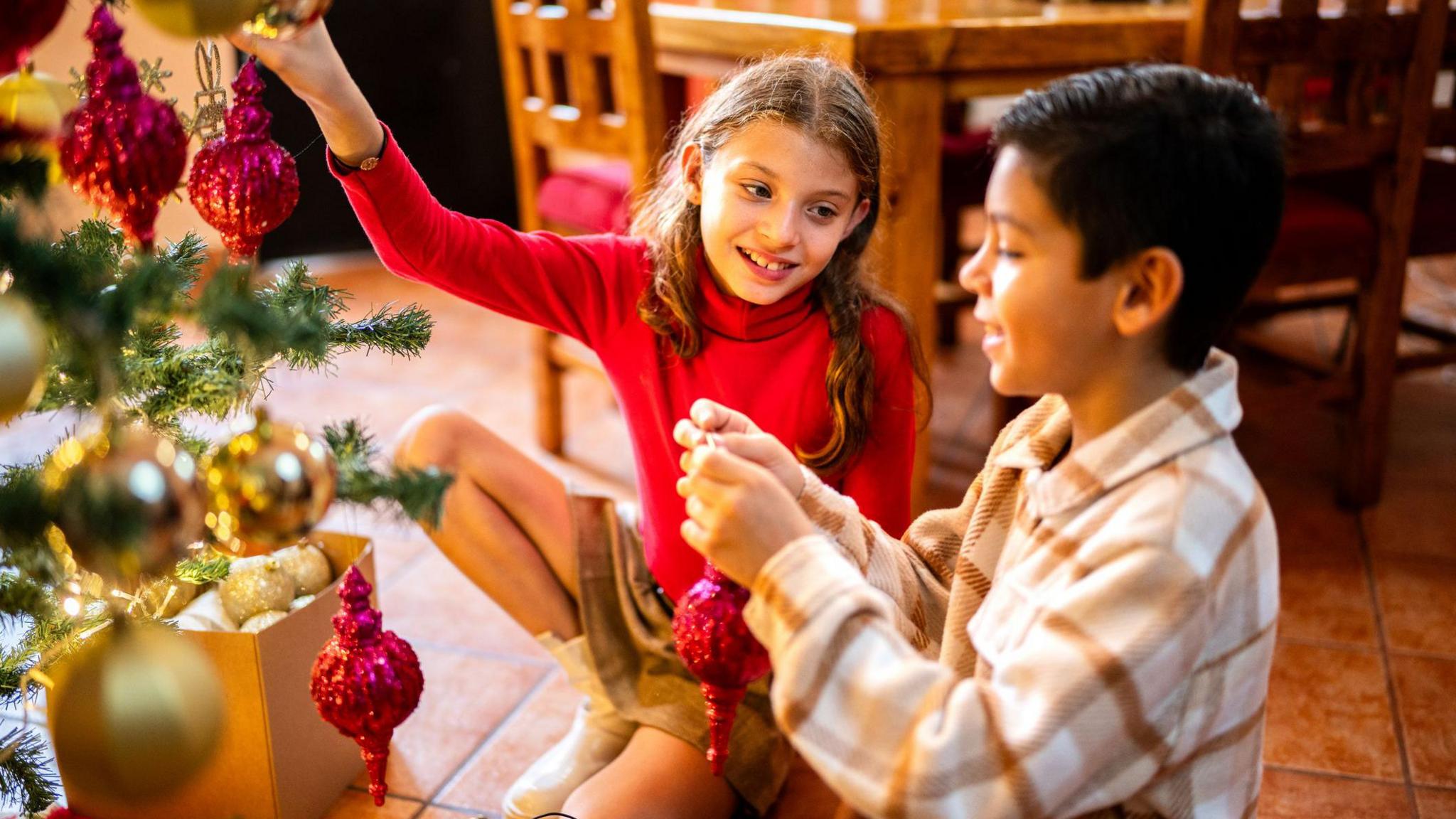 two children talking and decorating a Christmas tree.