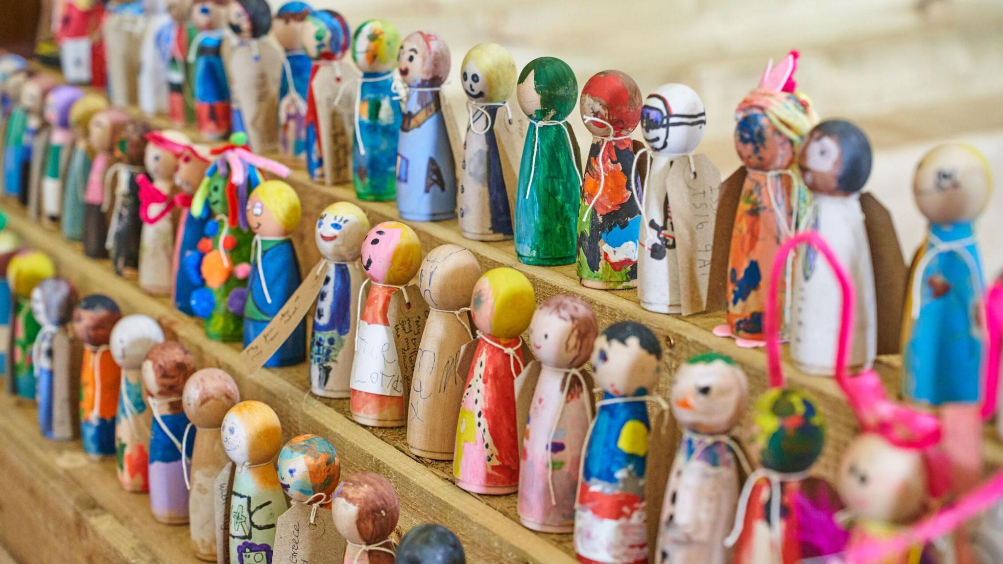 Three rows of small peg dolls in different colours. Some have drawings and messages written on them.