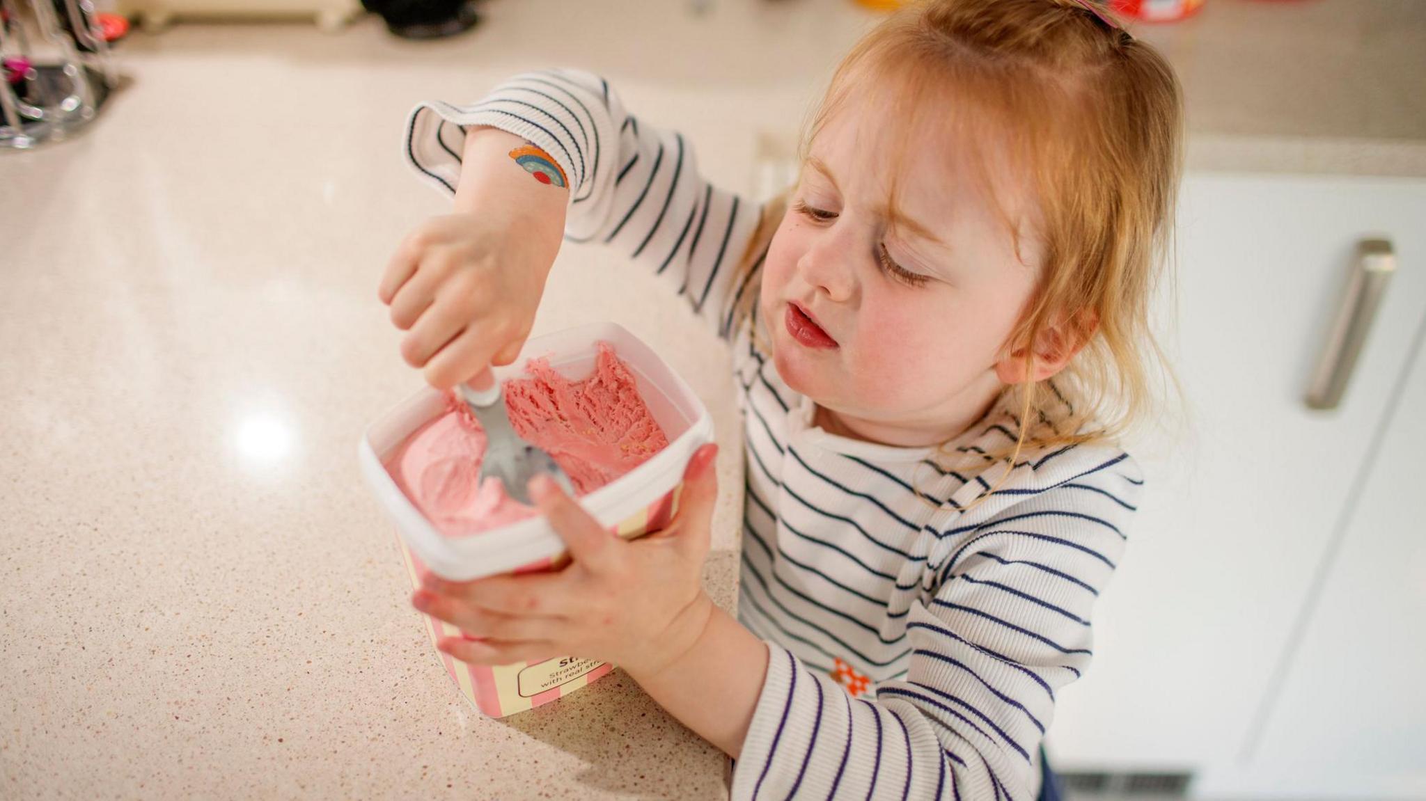 Girl eating ice cream from kitchen worktop