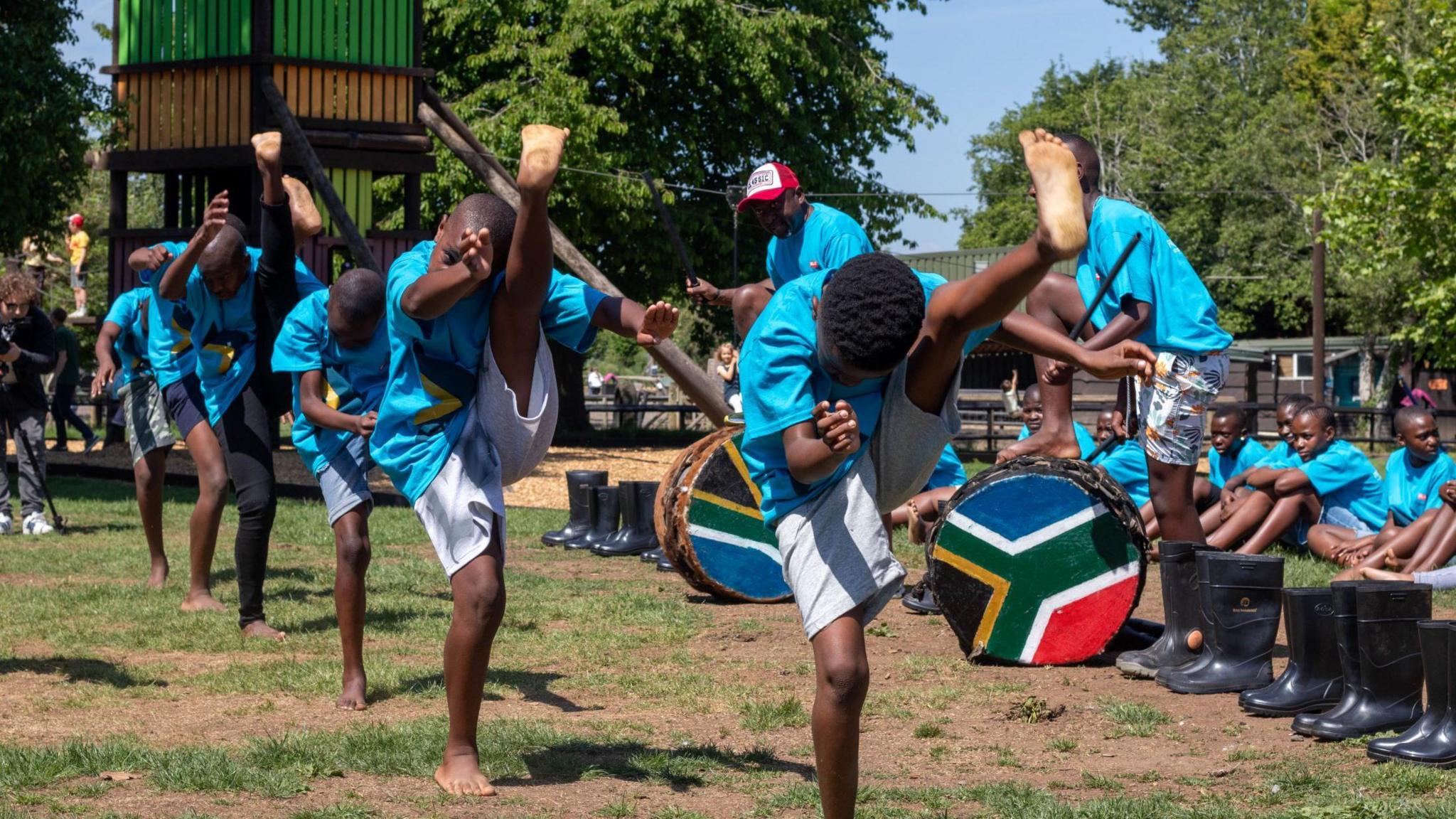 A group of Zulu dancers perform their moves at the Avon Valley Adventure Park in Bristol. They are all wearing blue T-shirts and are being watched by other members of their group
