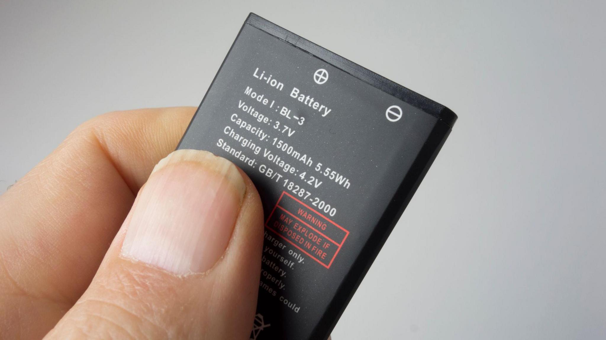 A thumb and finger holding a lithium-ion battery against a grey background